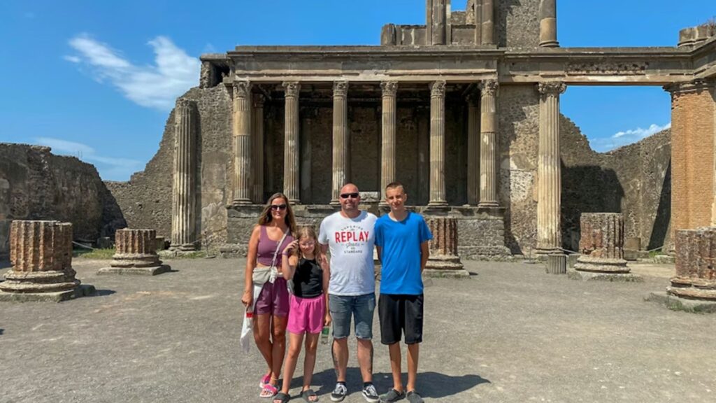 A family stands together smiling in front of the ancient ruins of Pompeii, capturing a moment of history and togetherness.