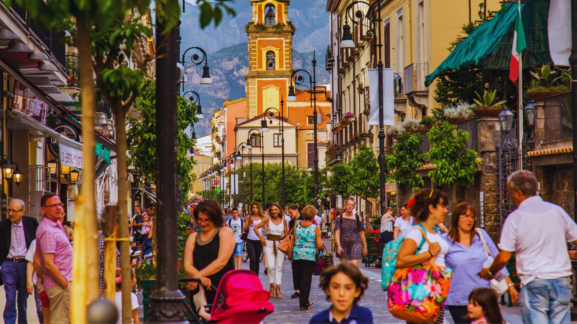 A bustling street scene filled with people walking and shopping among various storefronts and vibrant displays.