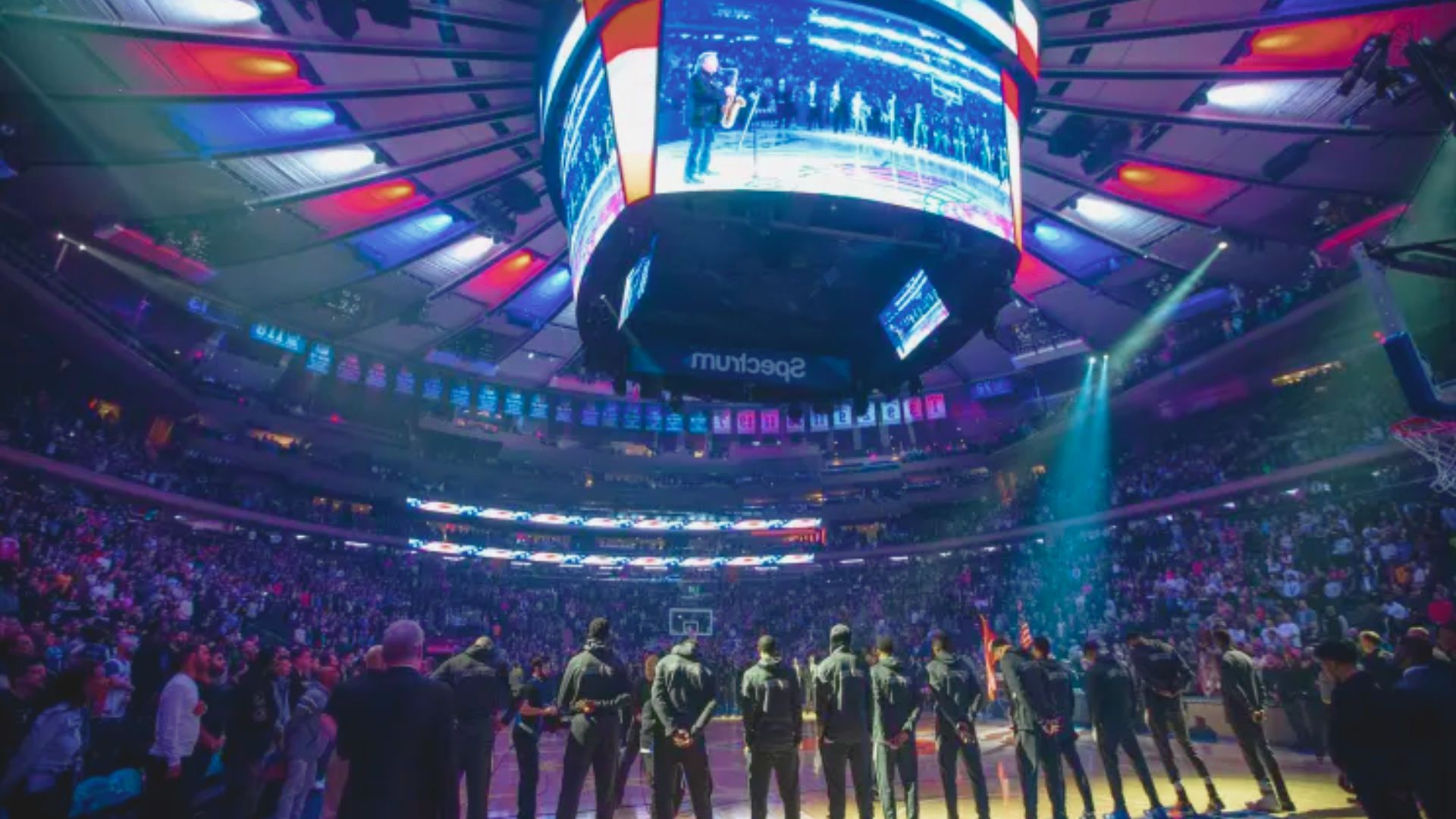 The Knicks stand on the court, facing a large screen displaying game highlights and team graphics.