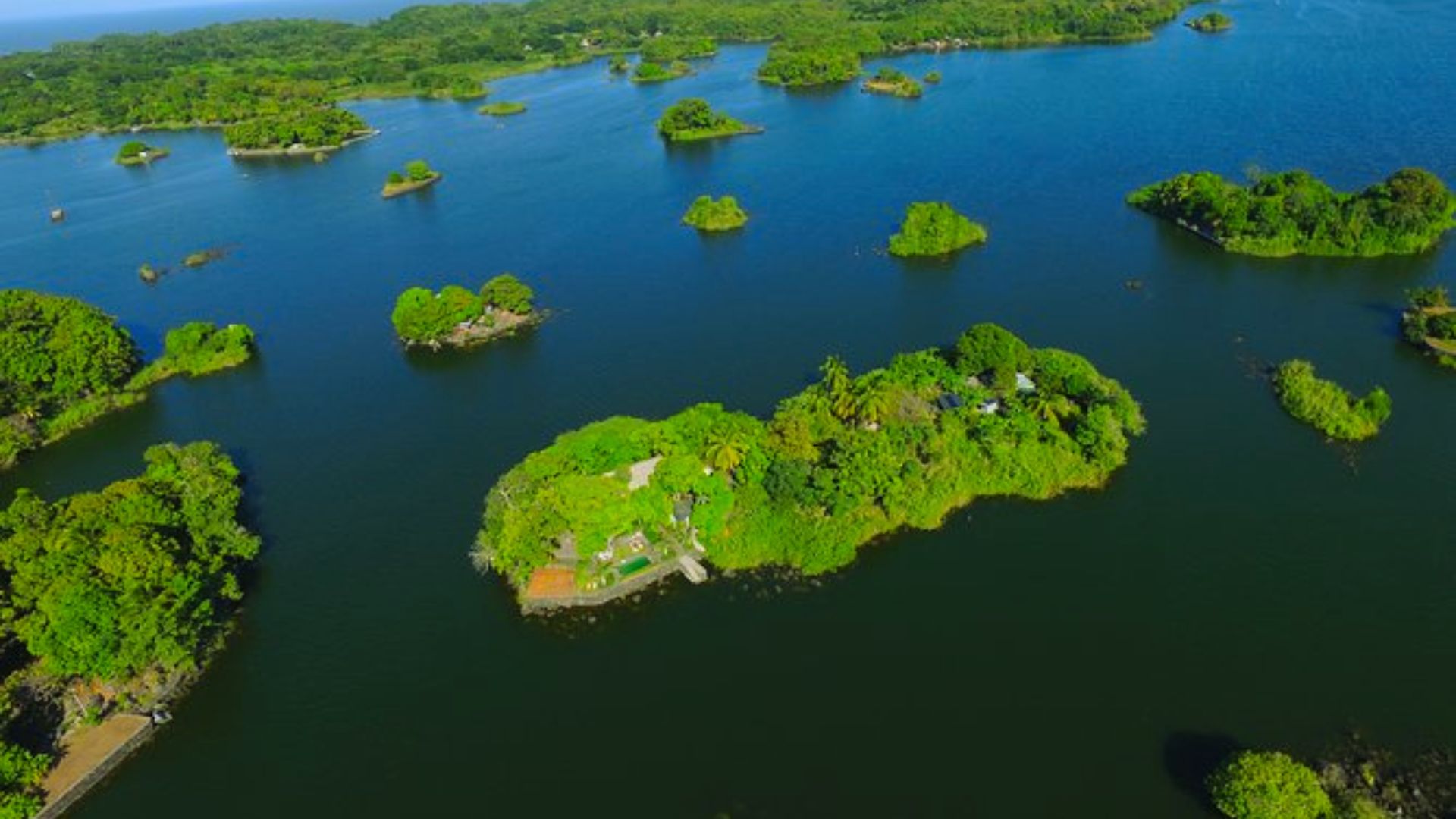 Aerial view of lush green islands scattered across a vast blue lake, creating a serene and peaceful landscape. The scene exudes tranquility and natural beauty.