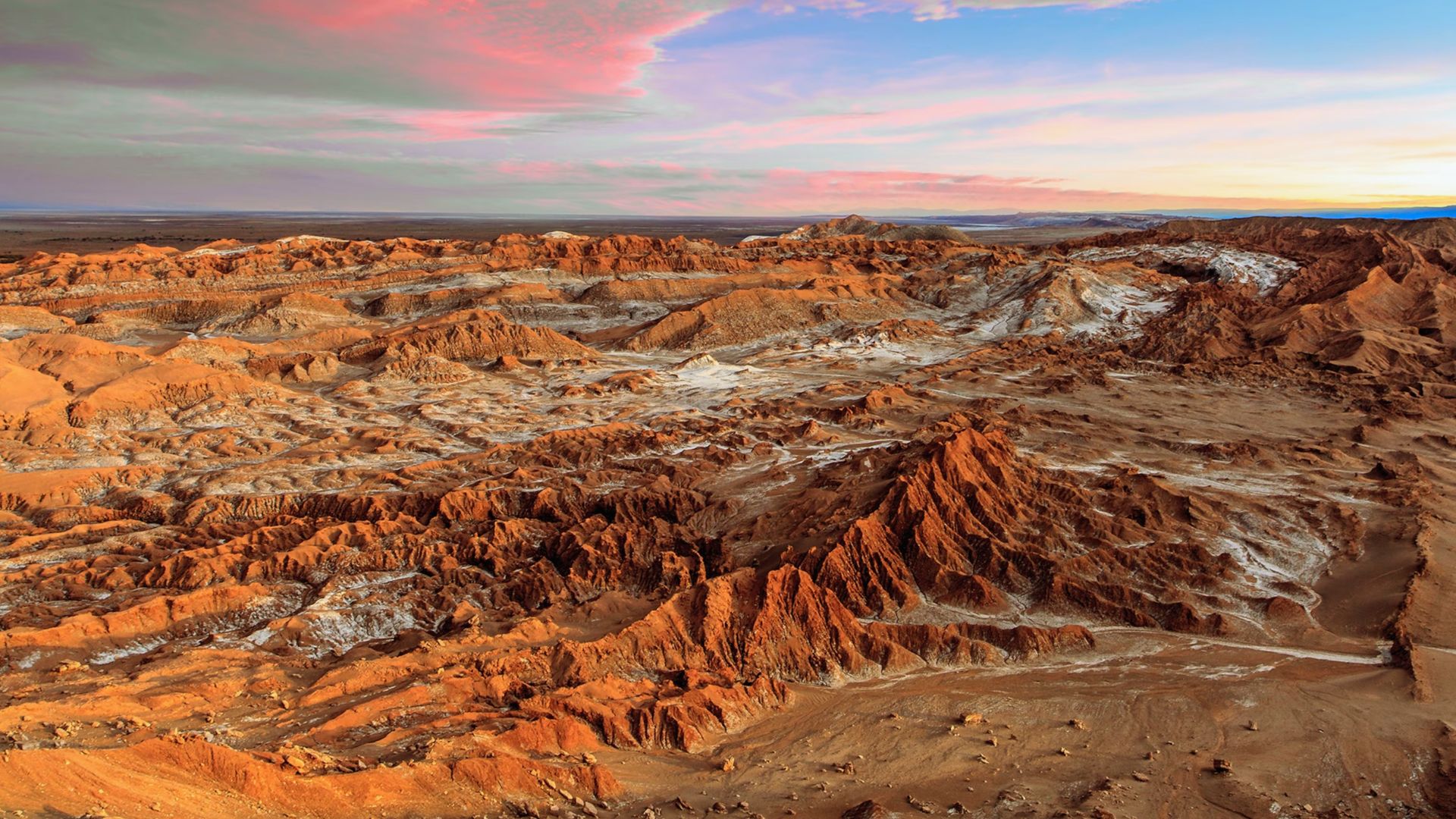 A vast desert landscape featuring an expanse of red rocks under a clear blue sky.