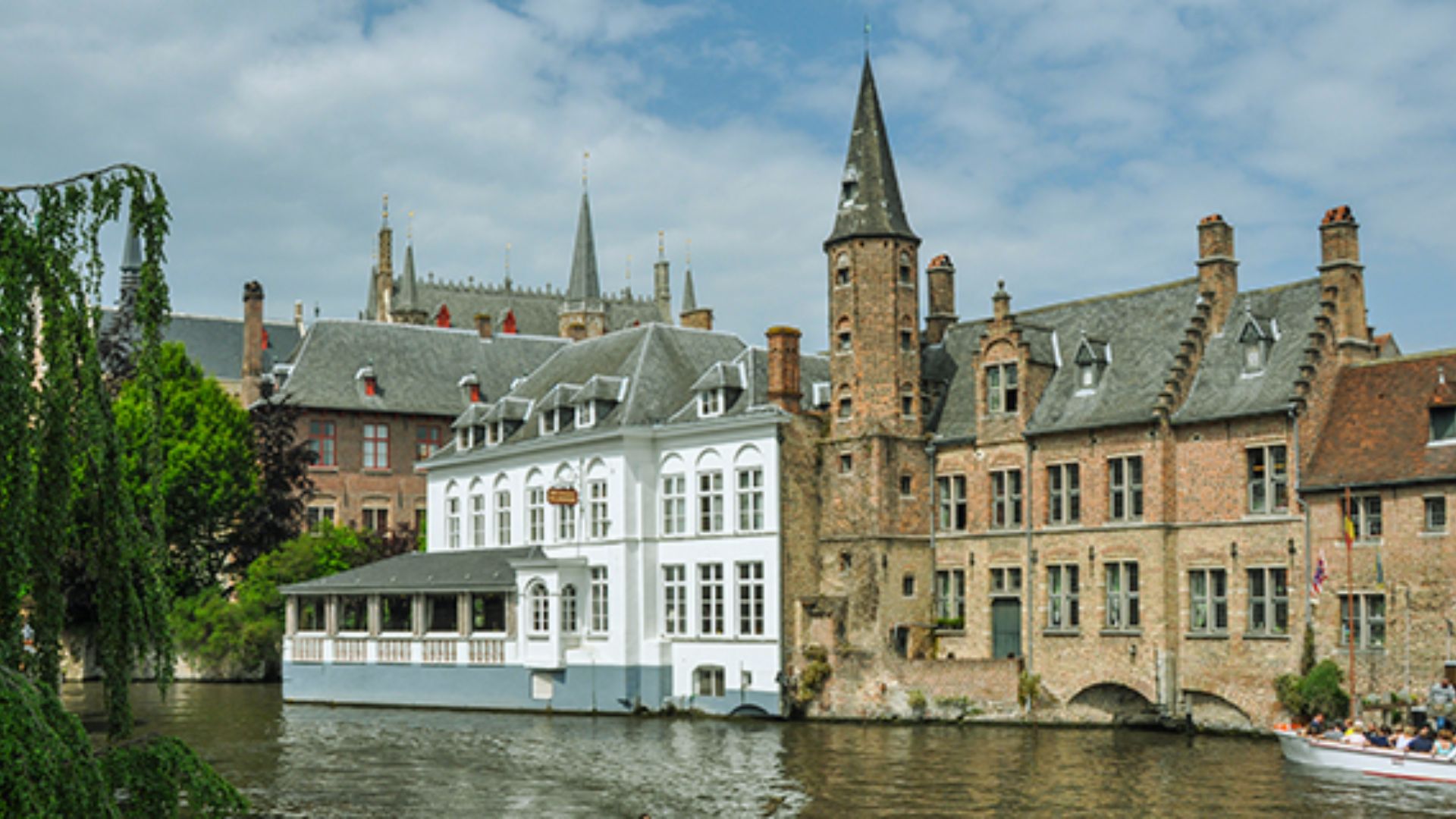 A boat glides down a river, with a building visible in the background.