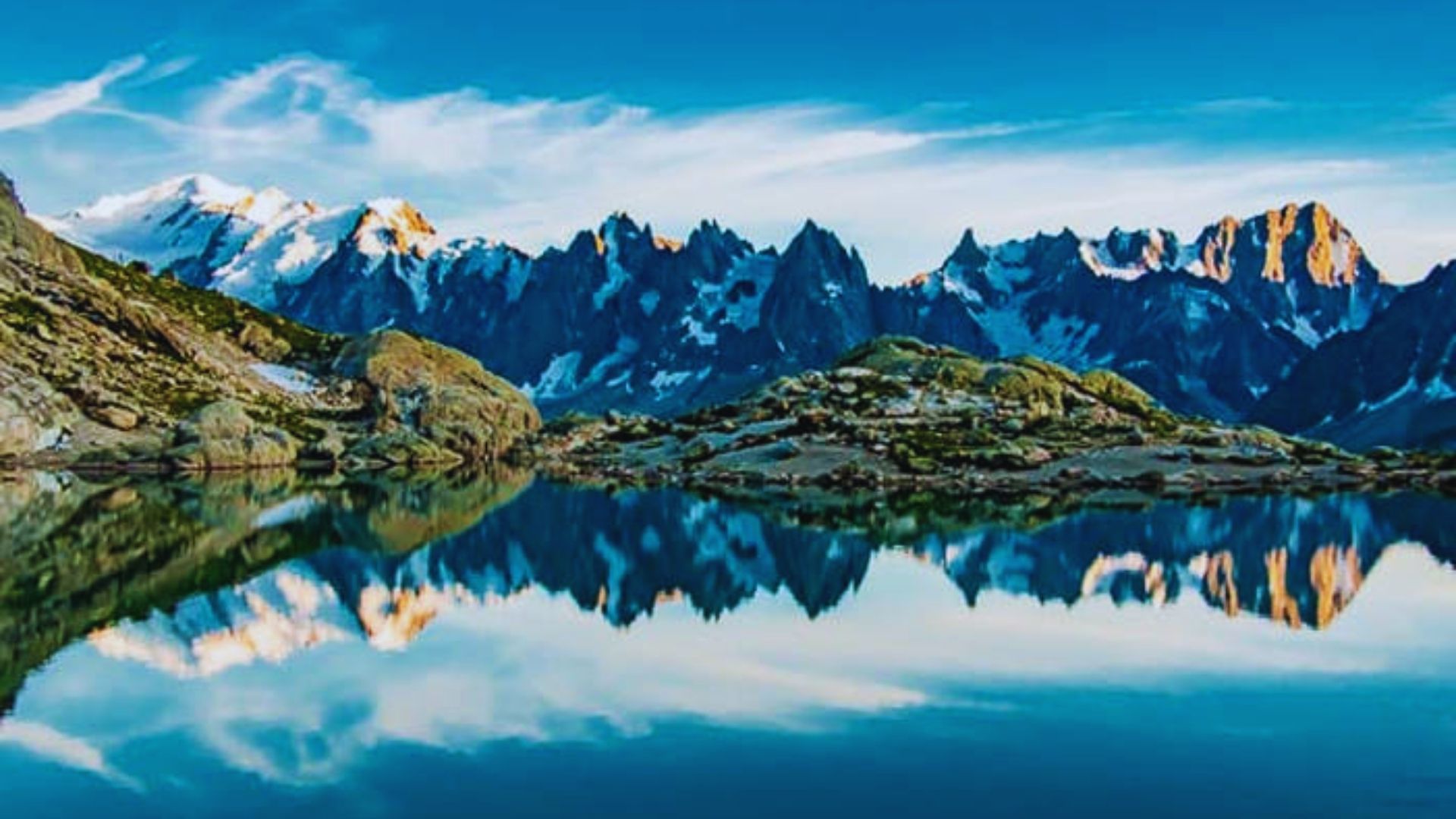 Serene mountains reflected in a calm lake under a clear blue sky, creating a picturesque natural landscape.
