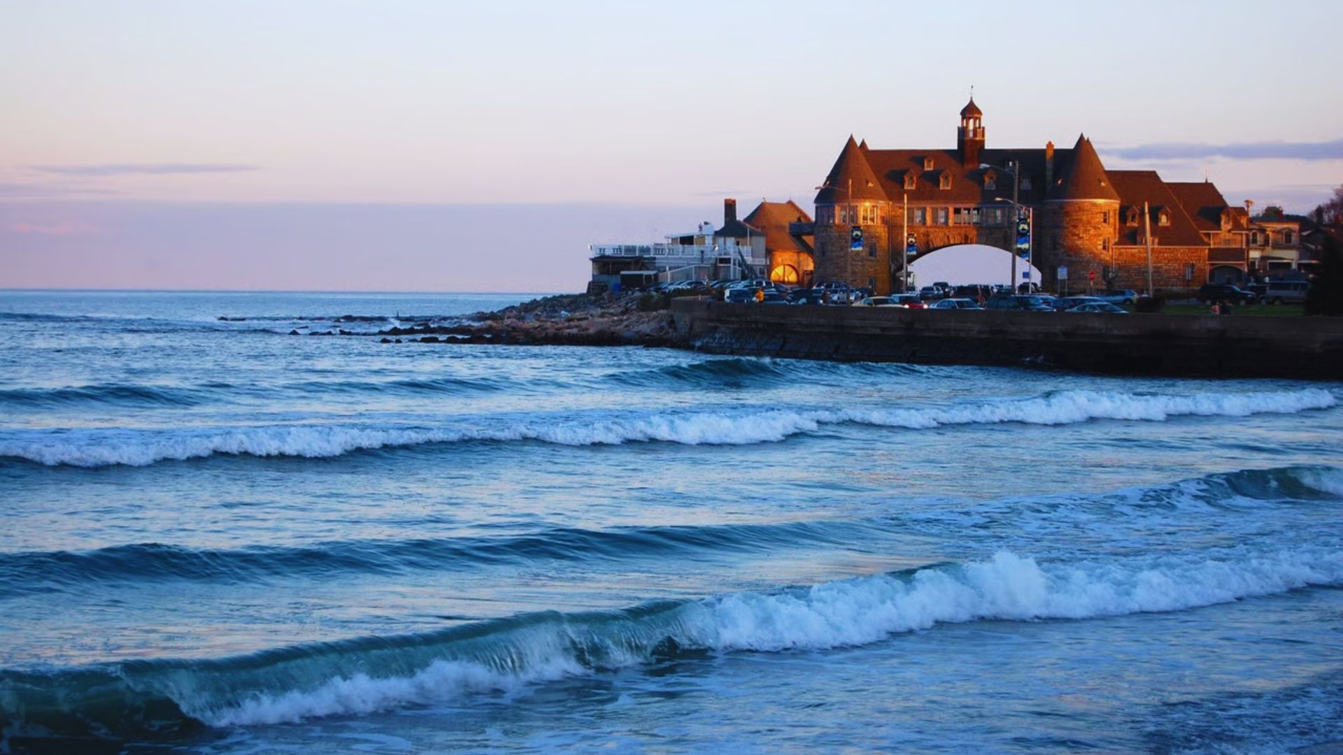 . A majestic castle overlooks the ocean, perched on a rocky shore under a clear blue sky.