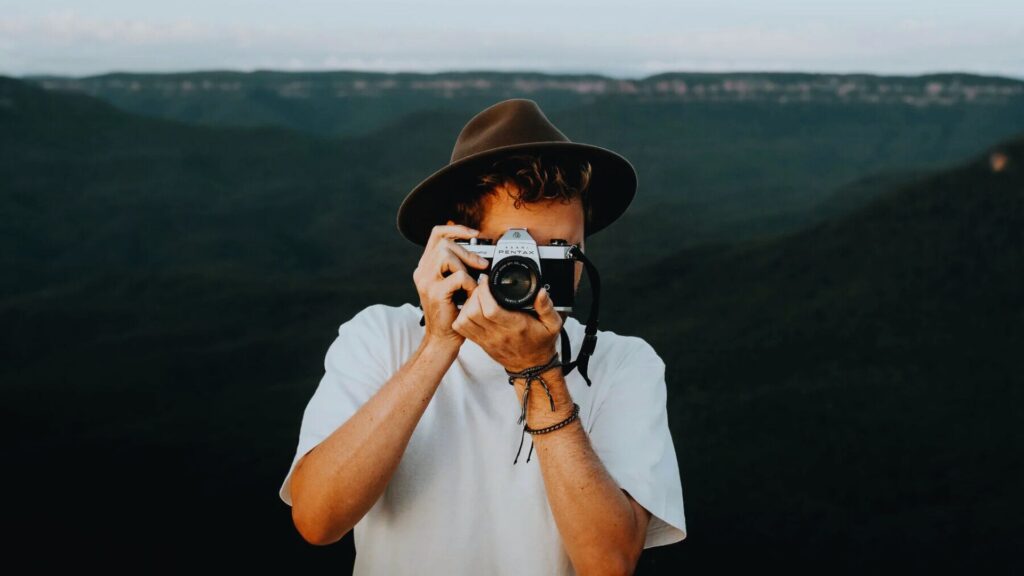 Man photographing mountains with a camera, capturing the scenic landscape in the background.