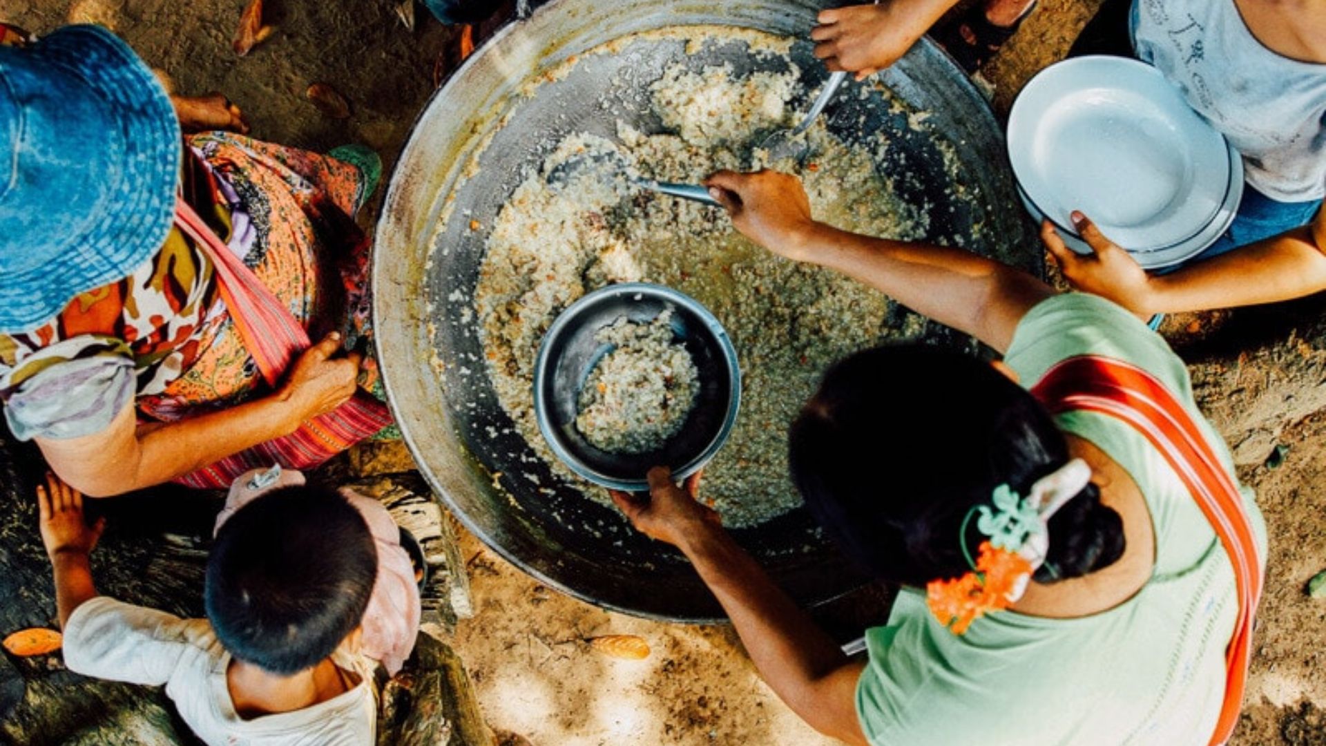 People are preparing food together in a large bowl, mixing ingredients with enthusiasm and collaboration.