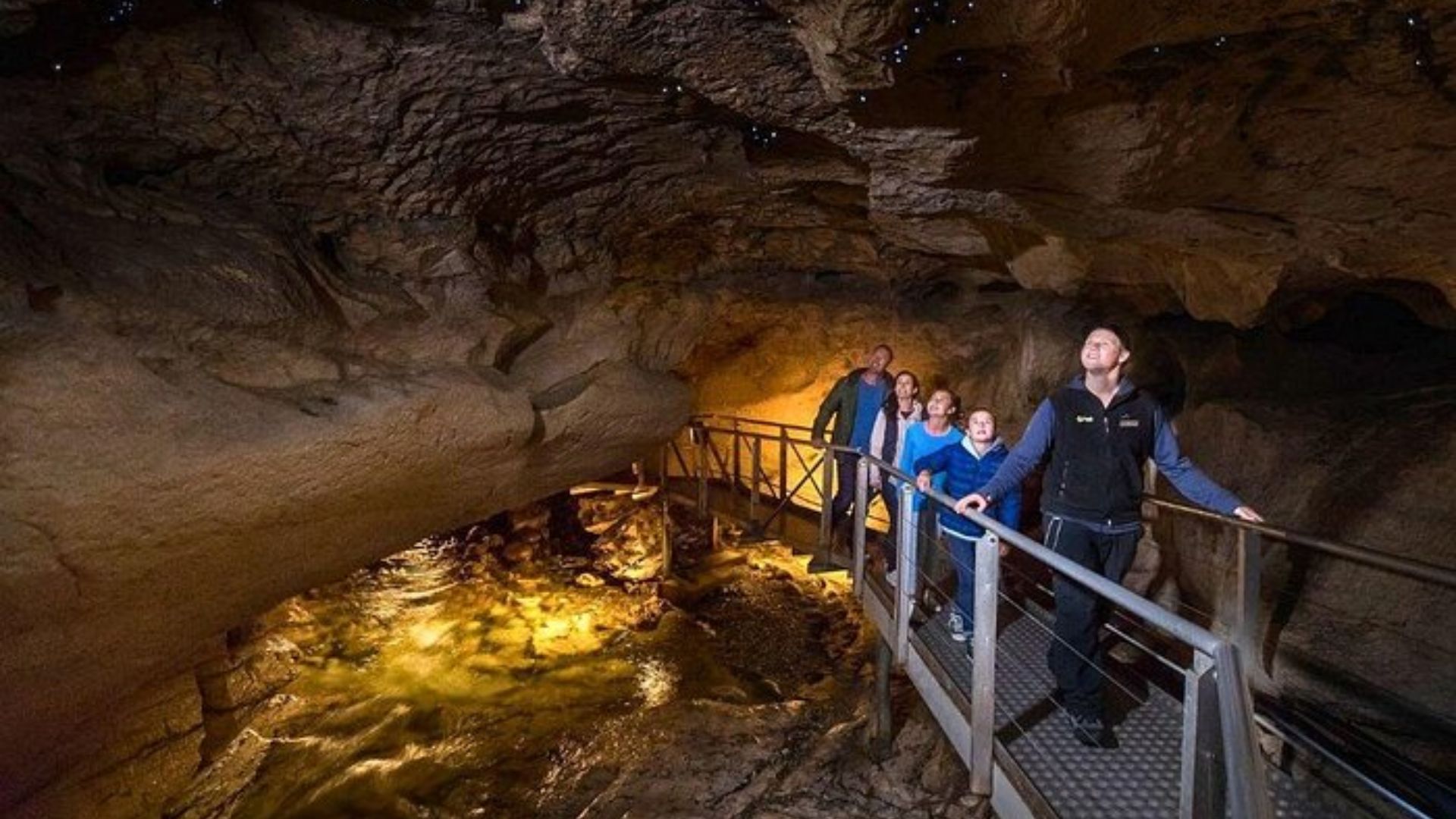 People walking through a dim cave, illuminated by a bright light shining on them from above.