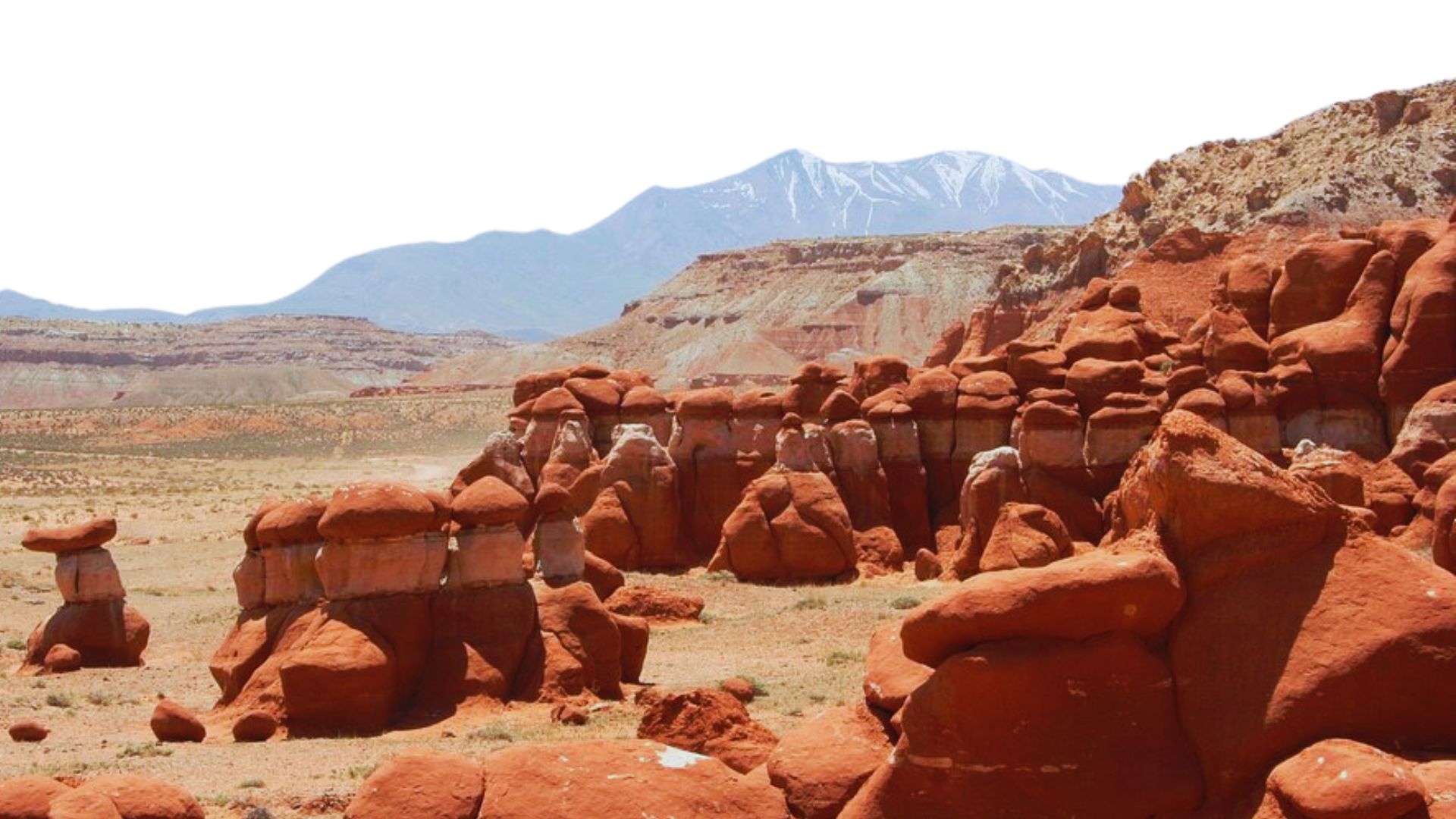 Red rocks in a desert landscape with distant mountains rising against a clear blue sky.