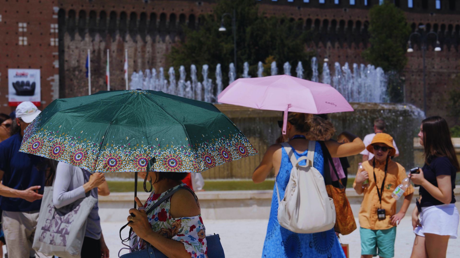 A group of people walking outdoors, each holding colorful umbrellas against a cloudy sky.