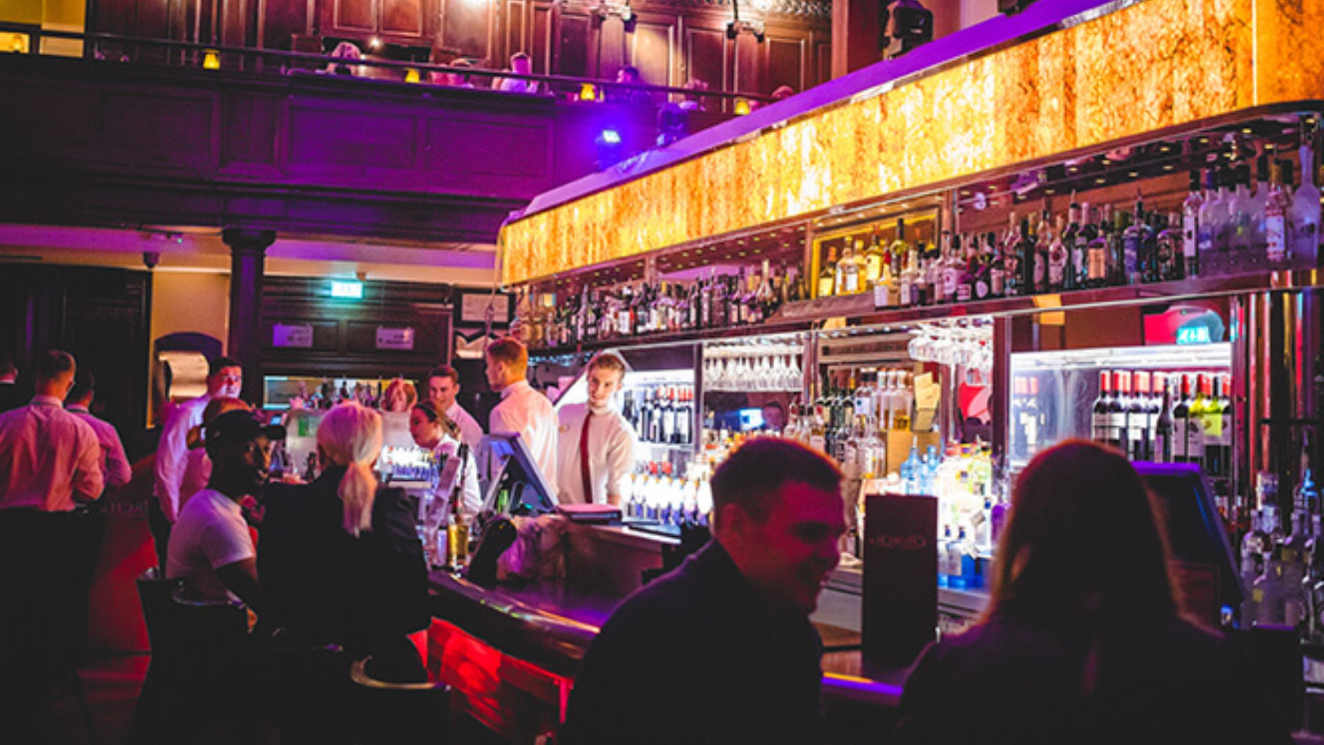 A diverse group of patrons gathered at a bar in a roomy setting, surrounded by a lively atmosphere.