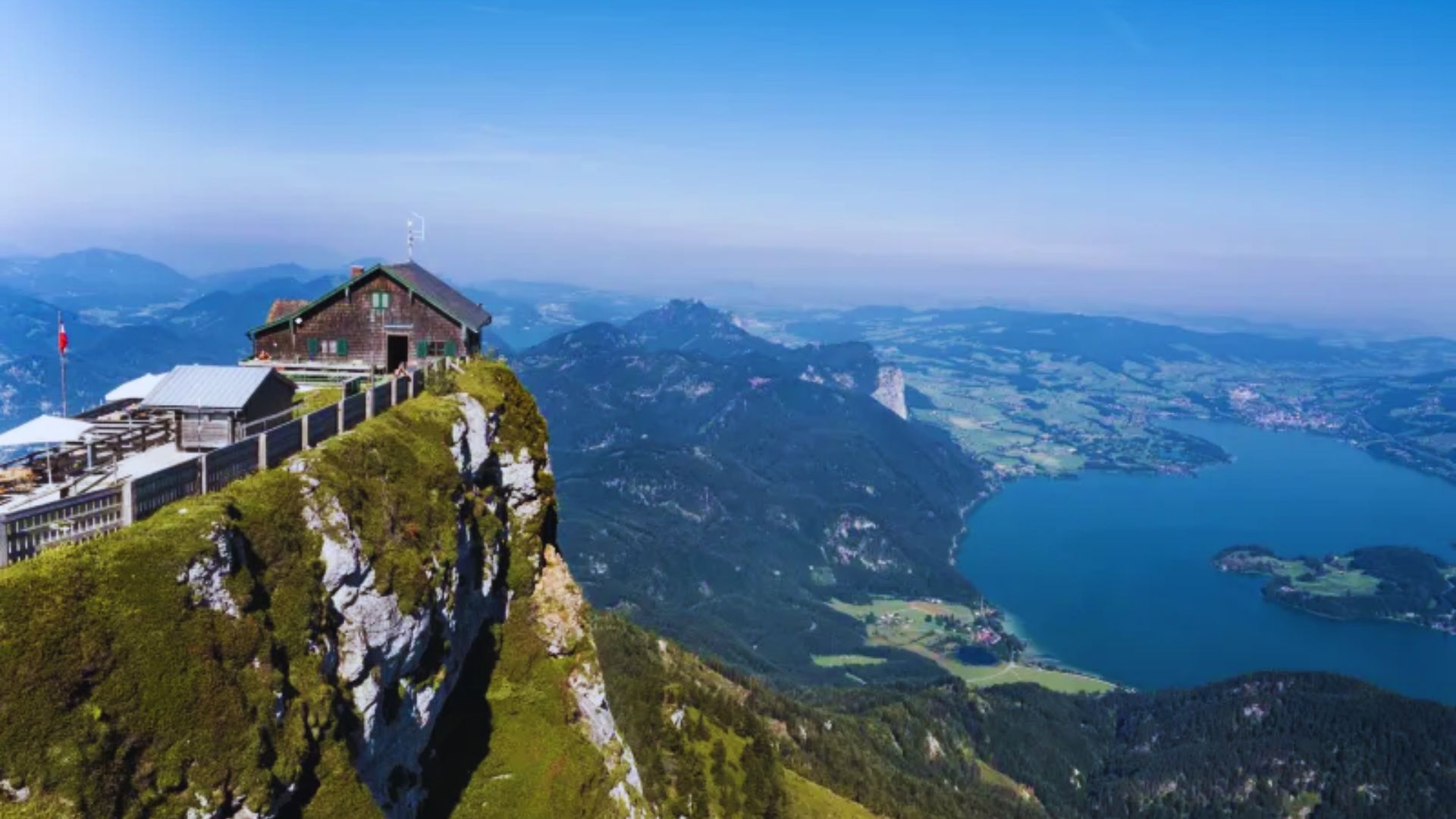 Panoramic view from the mountain summit, showcasing vast landscapes and distant peaks under a clear blue sky.