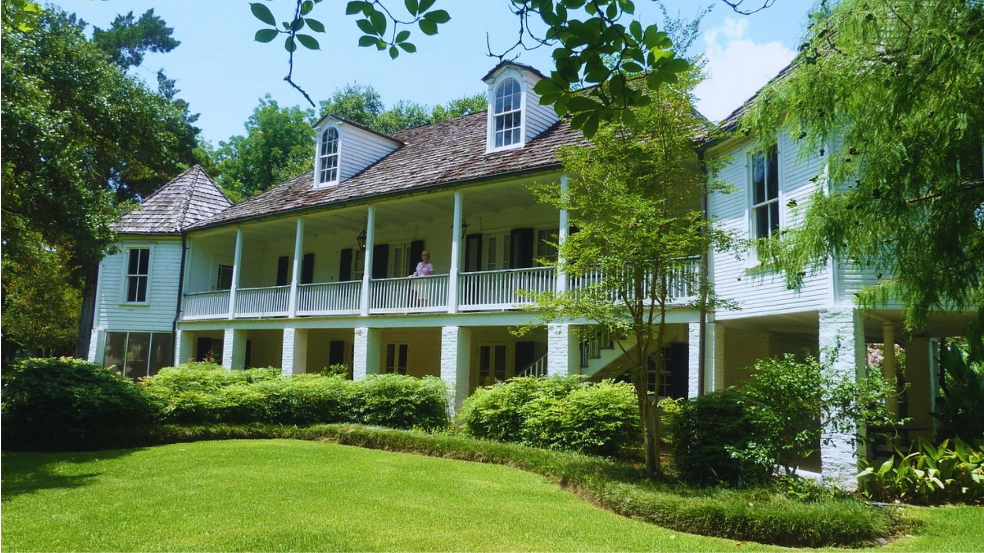 A white house featuring a spacious porch, surrounded by greenery