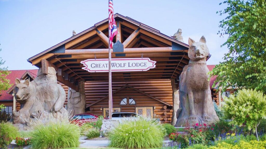 Complete Great Wolf Lodge Packing List Guide Entrance of Great Wolf Lodge, featuring large wooden wolf sculptures and a welcoming log cabin structure. Lush greenery surrounds the entrance.