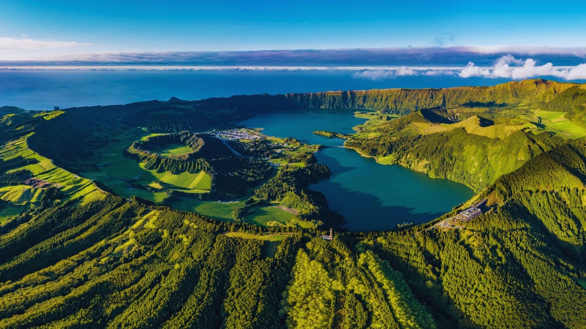 Aerial view of a Galapagos island showcasing a lake and a volcano surrounded by lush greenery and blue ocean waters.