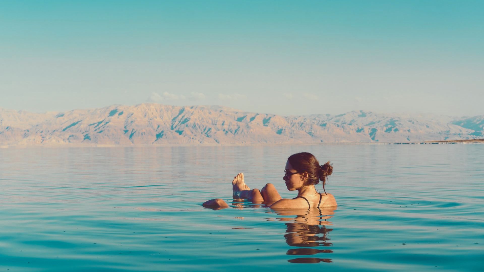 A woman effortlessly floating in the Dead Sea, surrounded by calm waters and a clear blue sky.