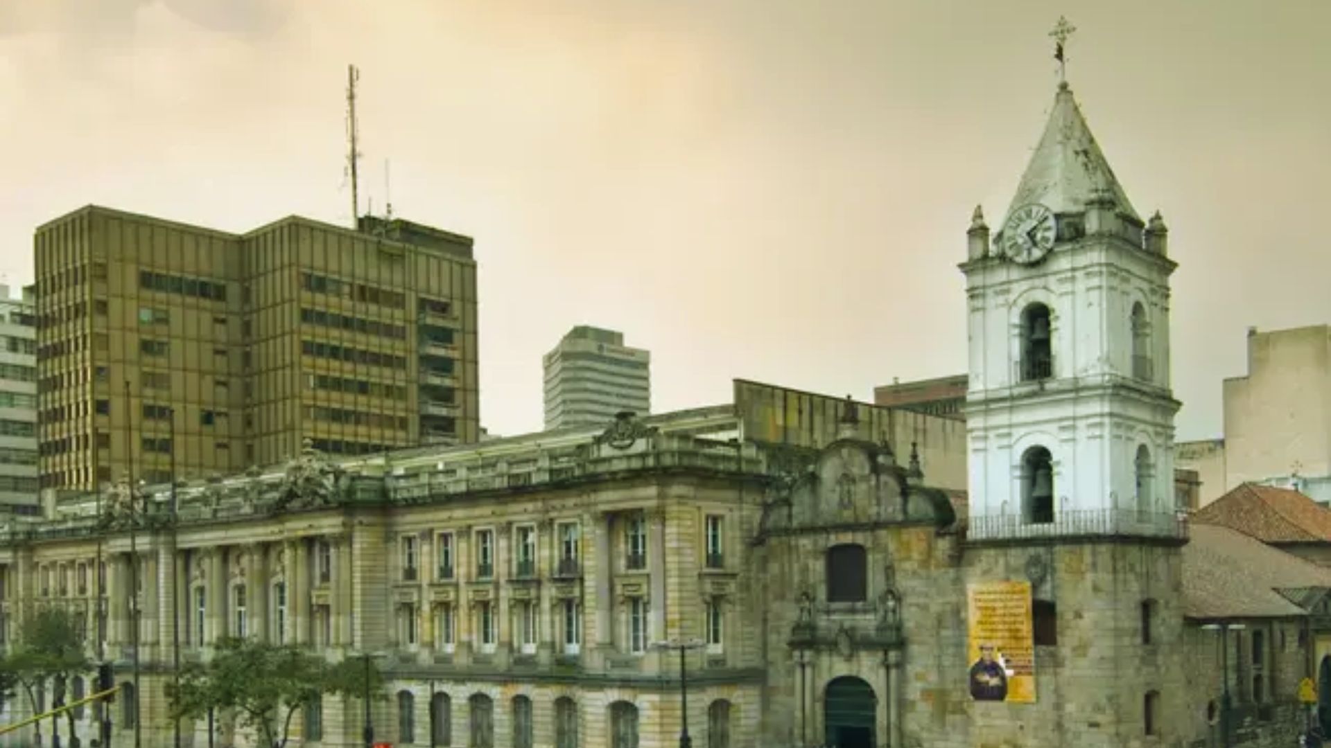 A large city building featuring a prominent clock tower at its center, surrounded by urban architecture.