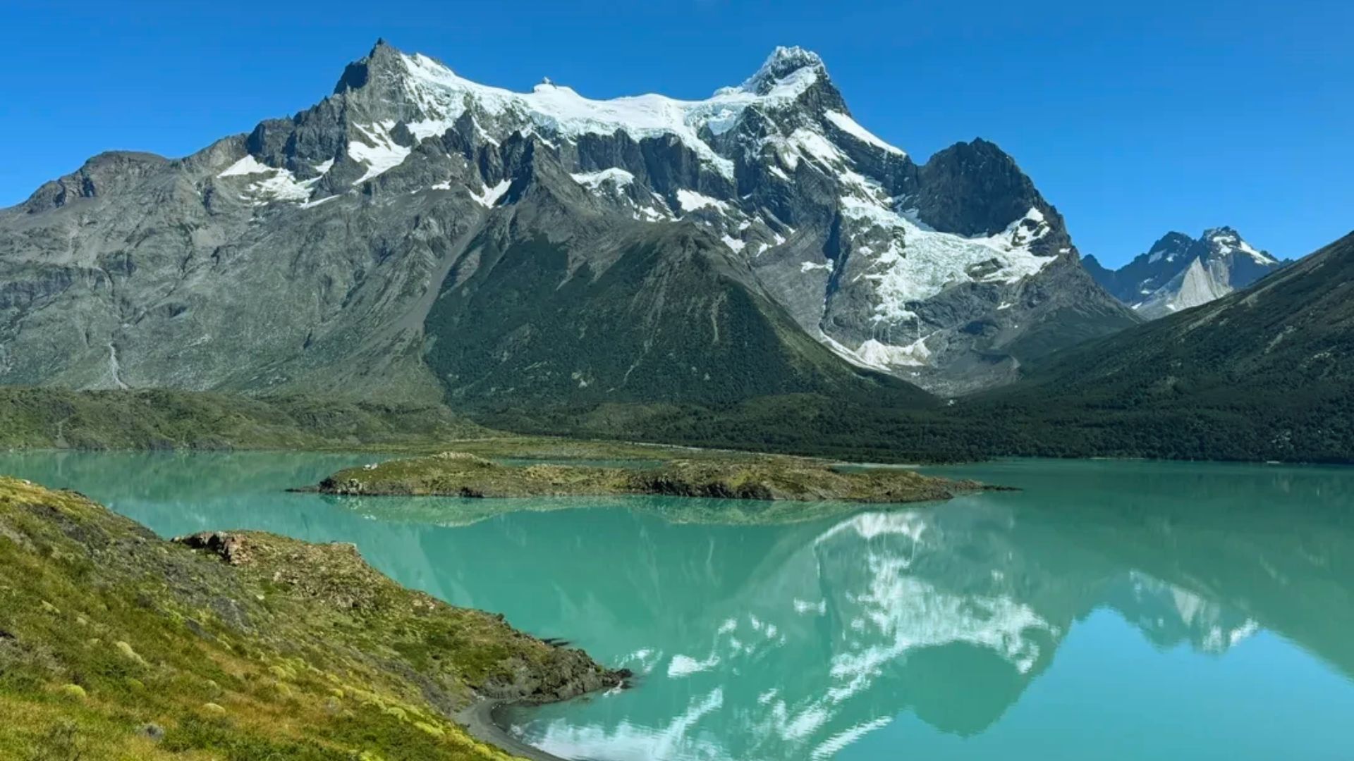 A stunning view of Patagonia's diverse landscape, featuring mountains, lakes, and lush greenery under a clear blue sky.
