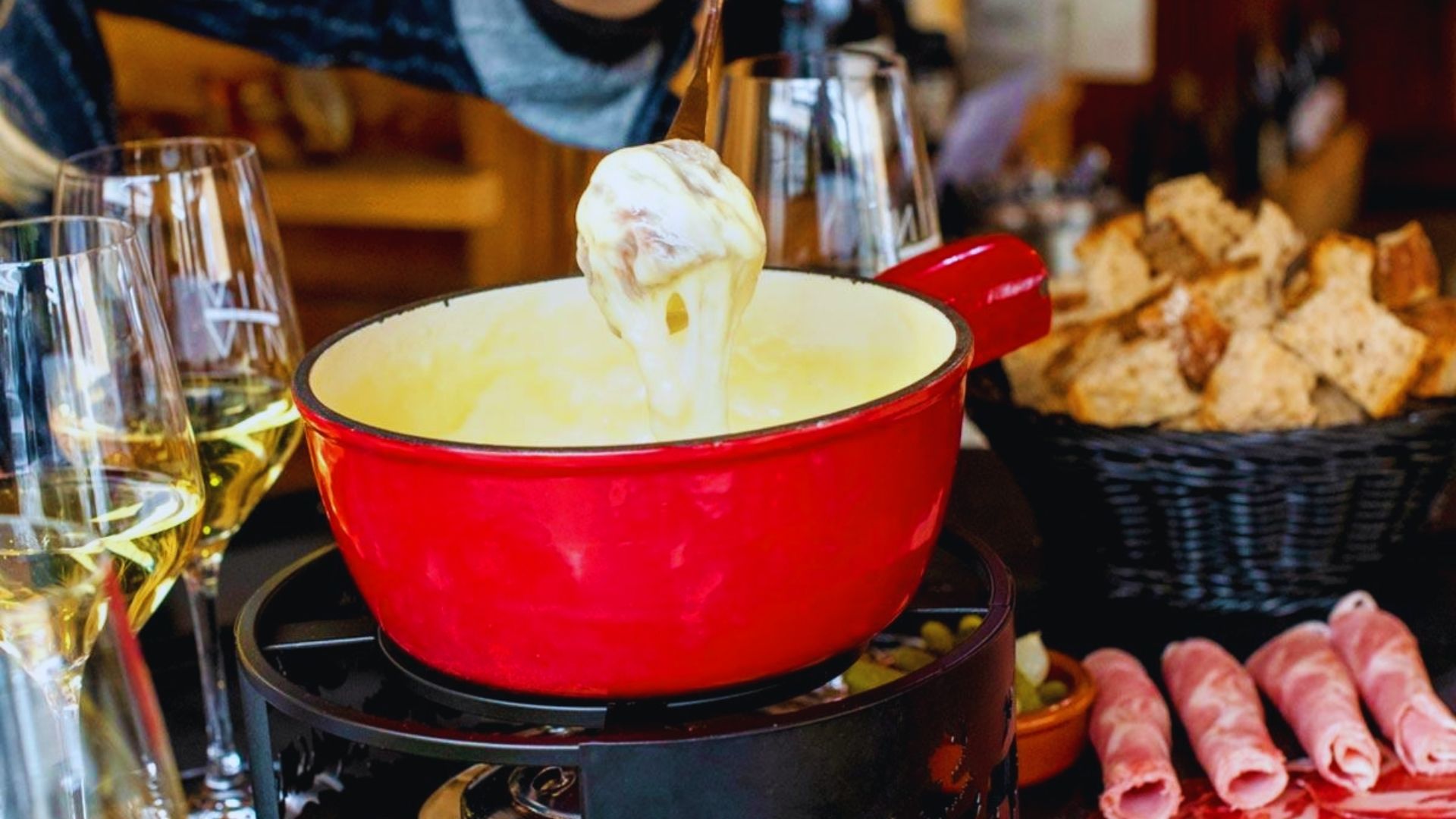 A person pouring melted cheese fondue into a pot, preparing for a communal dining experience.
