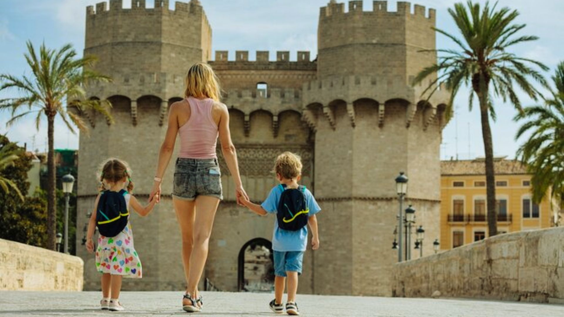 A woman walks with two children in front of a grand castle, creating a picturesque family moment.