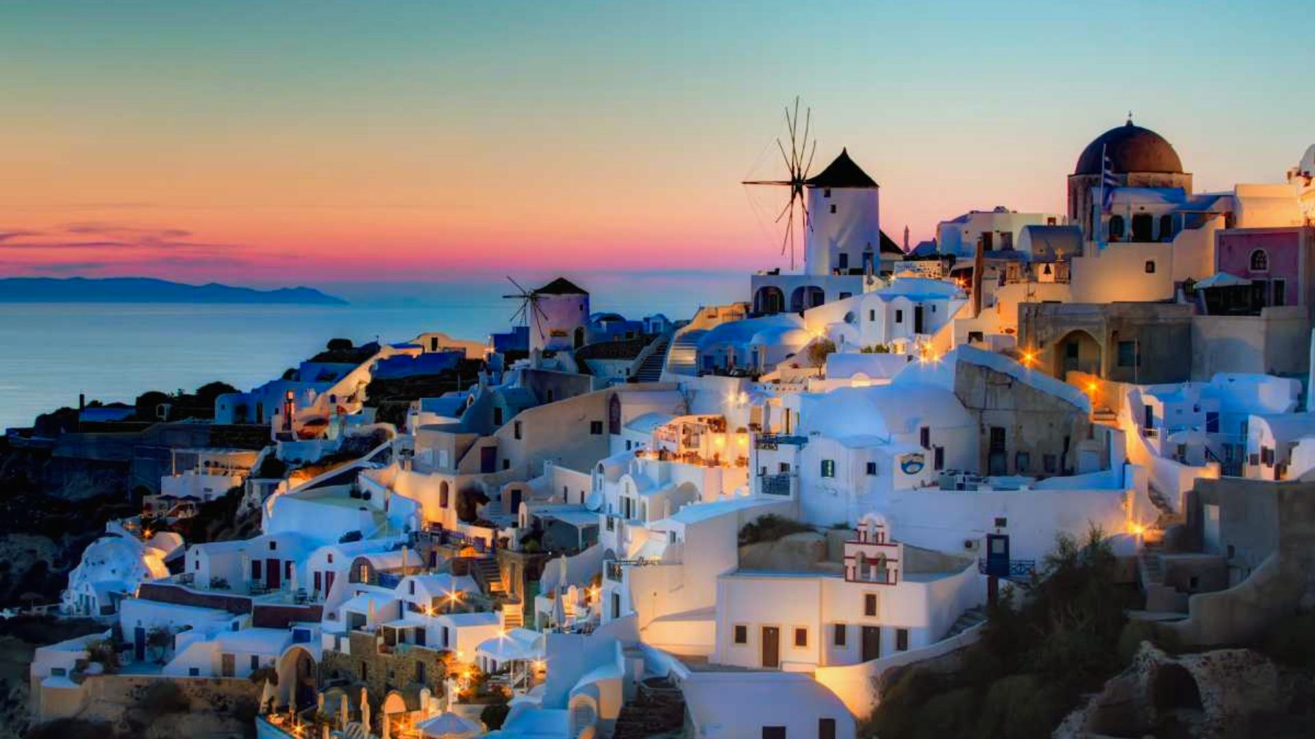 Sunset over Oia, Greece, casting warm hues across the town's iconic white buildings and blue-domed churches.