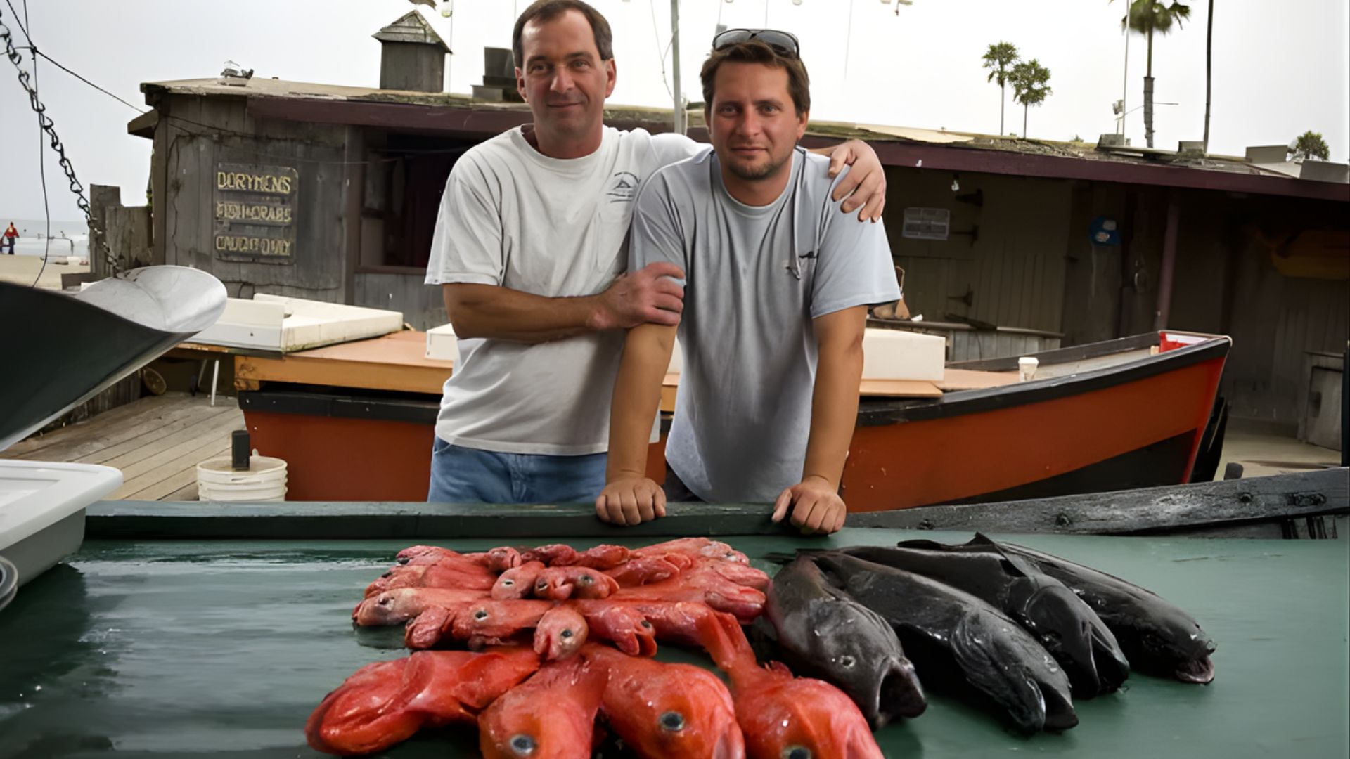 Two men smiling and posing with their catch of fish while standing on a boat.