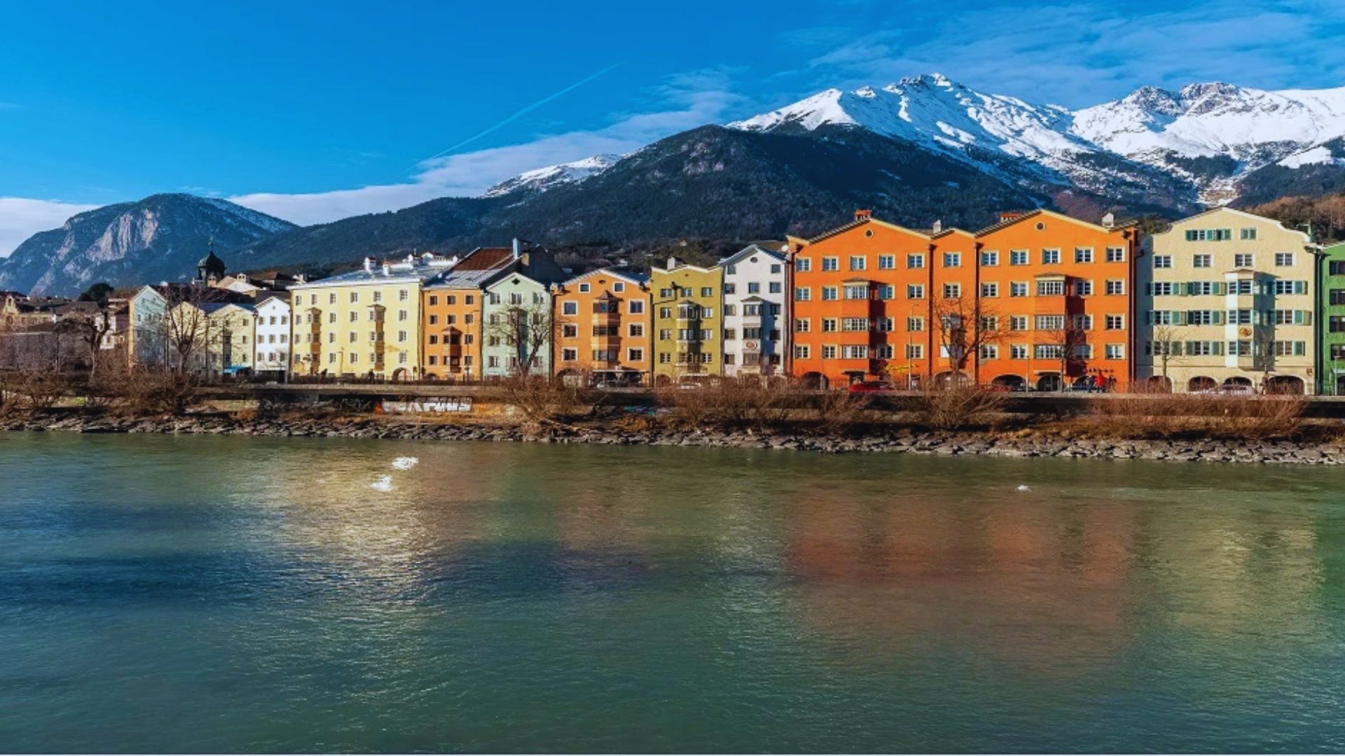Colorful buildings reflect along the riverbanks in Salzburg, creating a picturesque urban landscape.