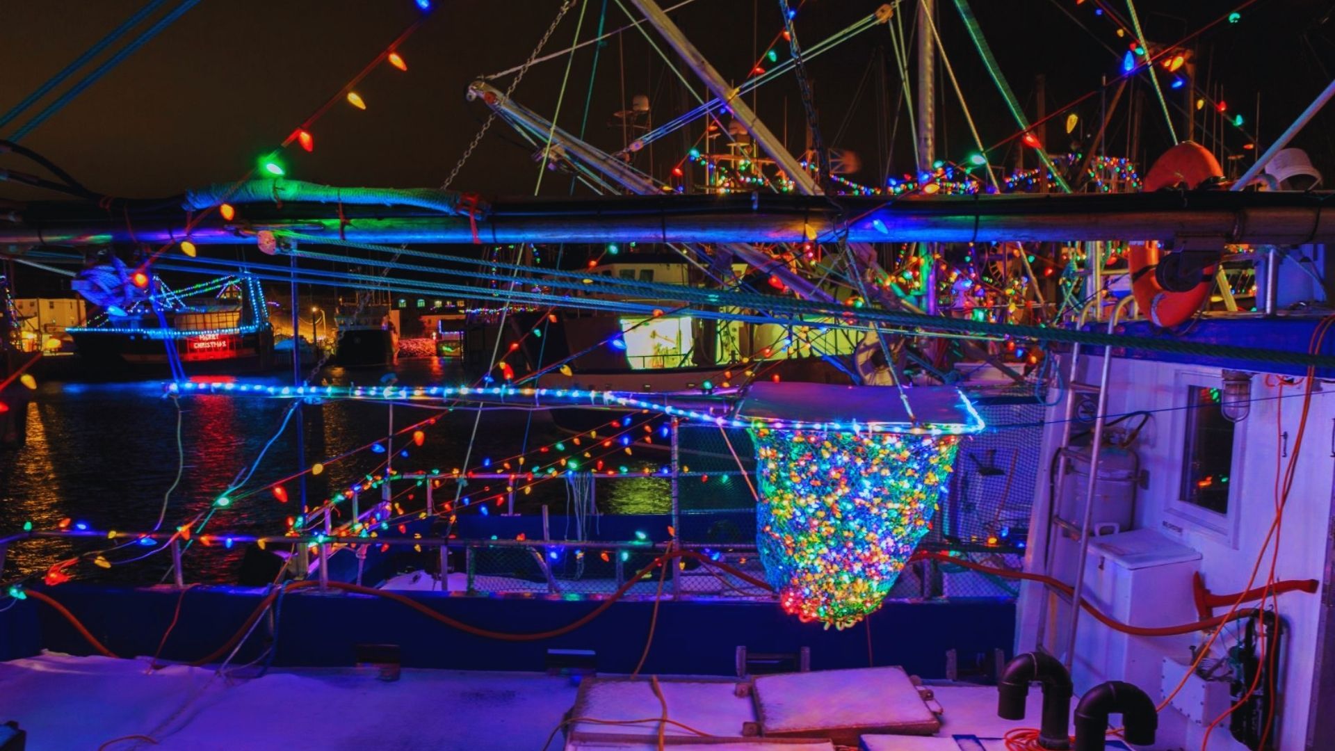 A boat adorned with colorful Christmas lights floating gently on the water at night.