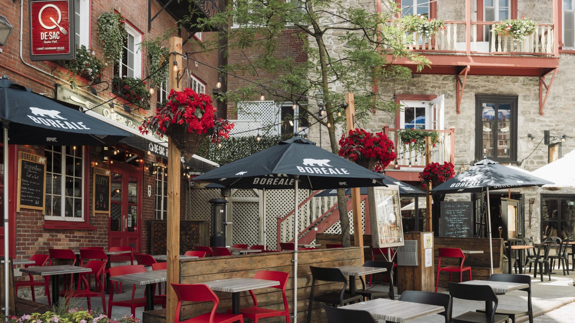 A sidewalk restaurant featuring red chairs and umbrellas, creating a vibrant outdoor dining atmosphere.