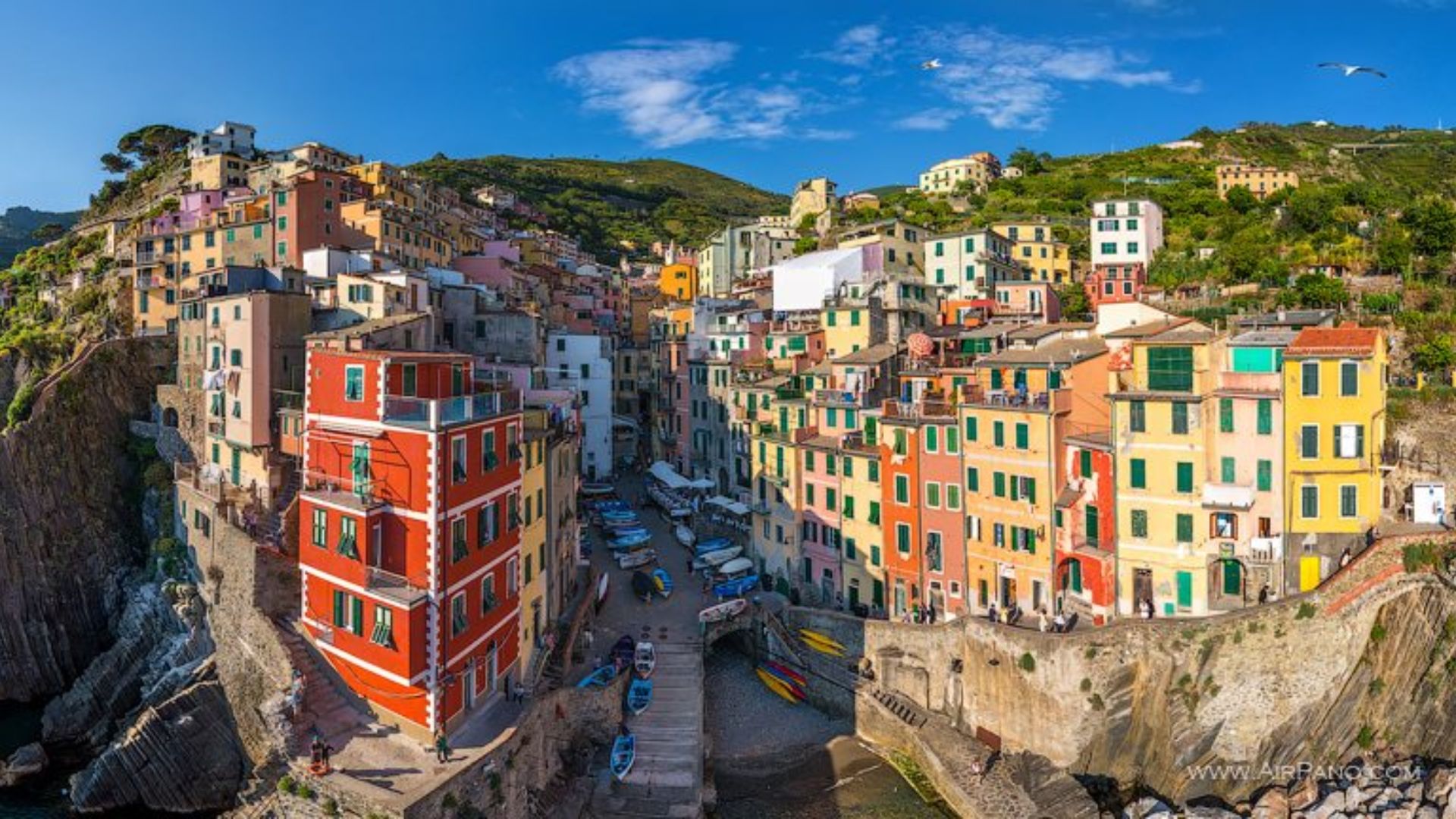 Colorful houses perched on a cliffside overlooking the vibrant Italian coast under a clear blue sky.