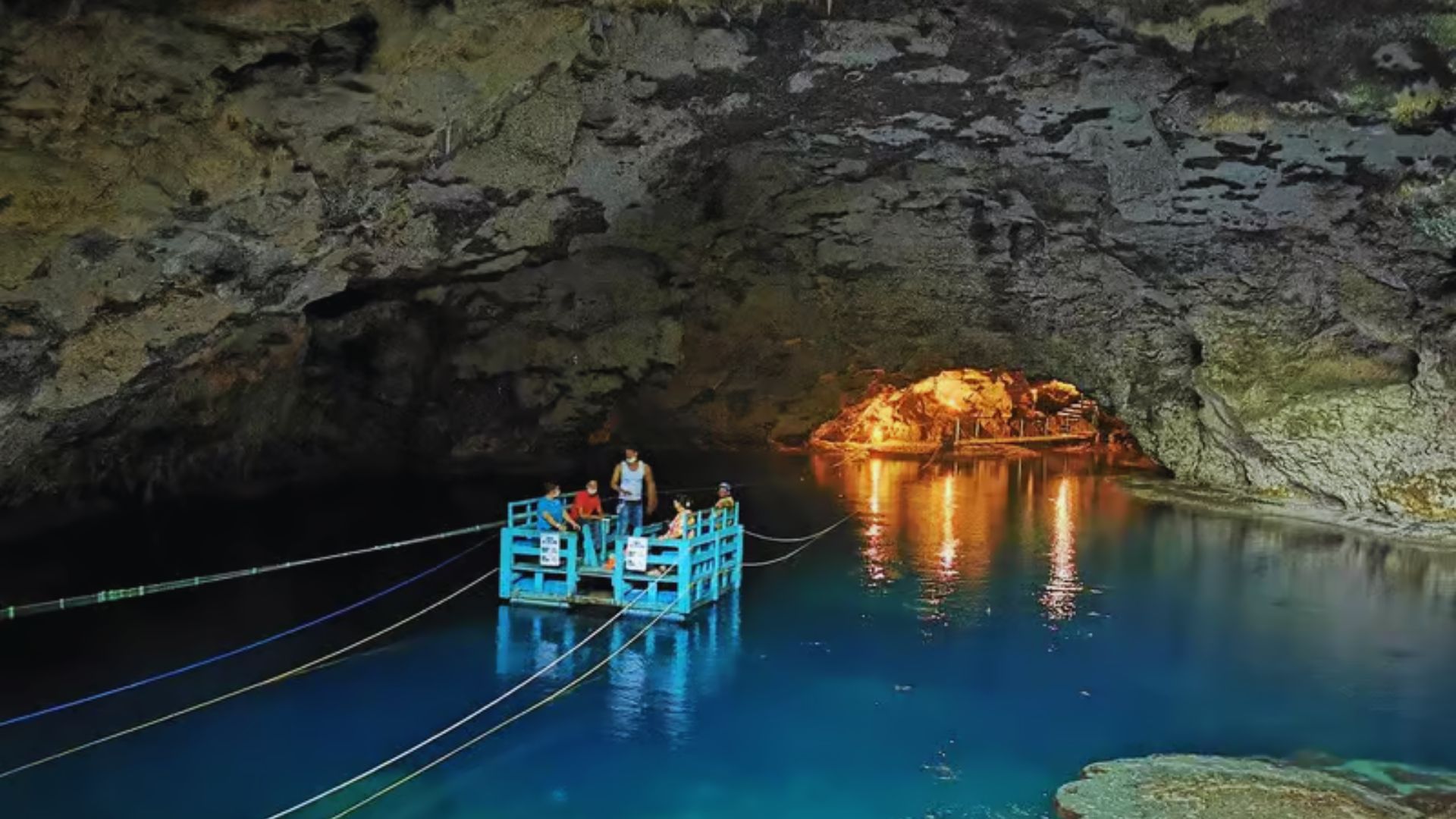 Individuals in a boat exploring a cave, with water flowing around them and rugged rock formations in the background.