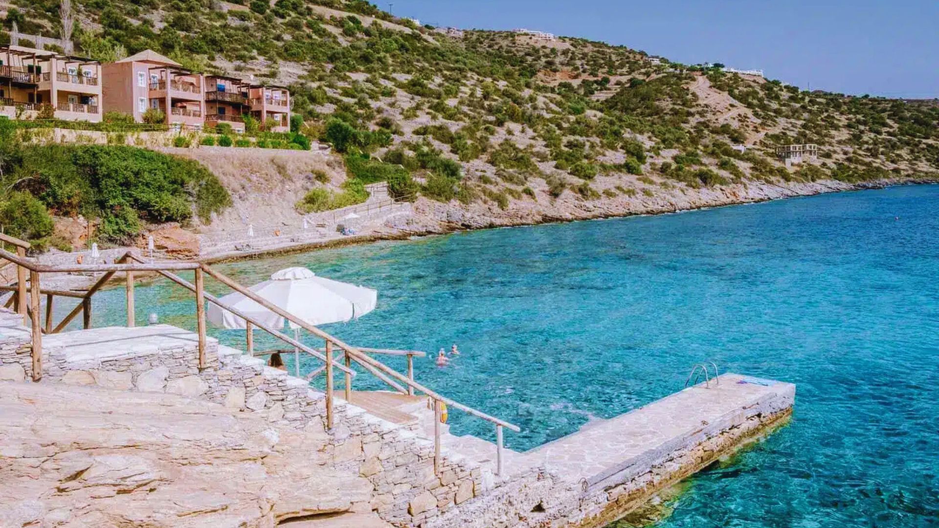 A scenic view of the beach and sea from a high cliff, showcasing waves crashing against the shore under a clear sky.