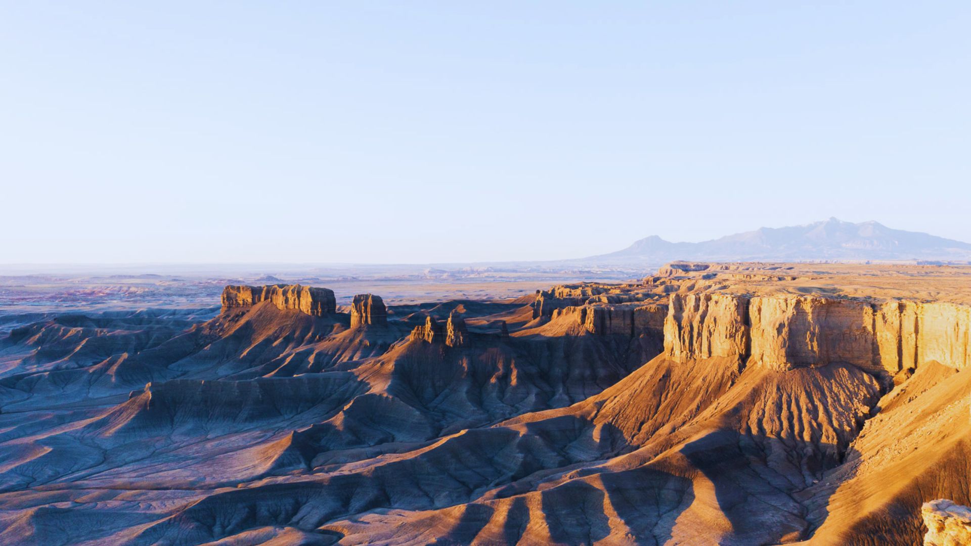 Expansive view of the Badlands in Arizona, showcasing rugged terrain and colorful rock formations under a clear blue sky.