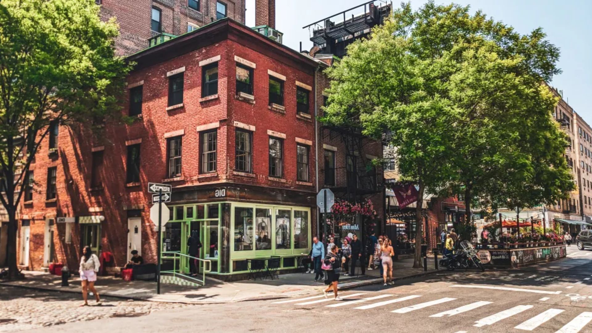 A bustling city street with pedestrians walking and standing on the sidewalk, surrounded by buildings and urban scenery.