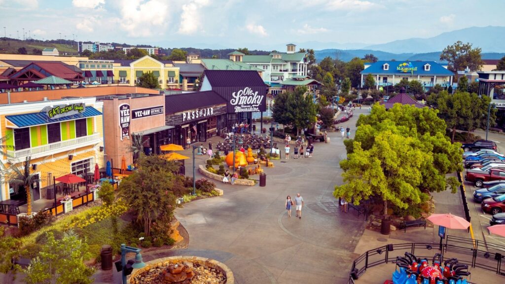 25 Hidden Things To Do in Pigeon Forge: Quiet Trails & Spots A vibrant shopping area with colorful buildings and crowded walkways. People are enjoying leisure activities. Trees and mountains are visible in the background.