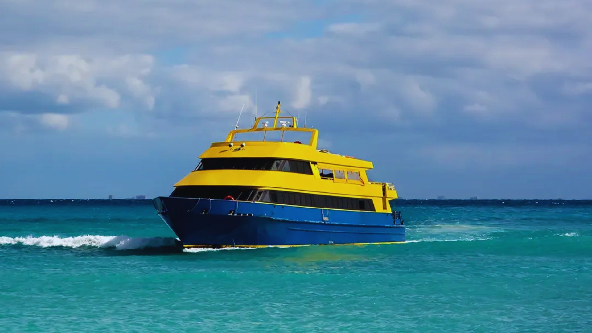A yellow and blue boat glides through the ocean waves under a clear sky.