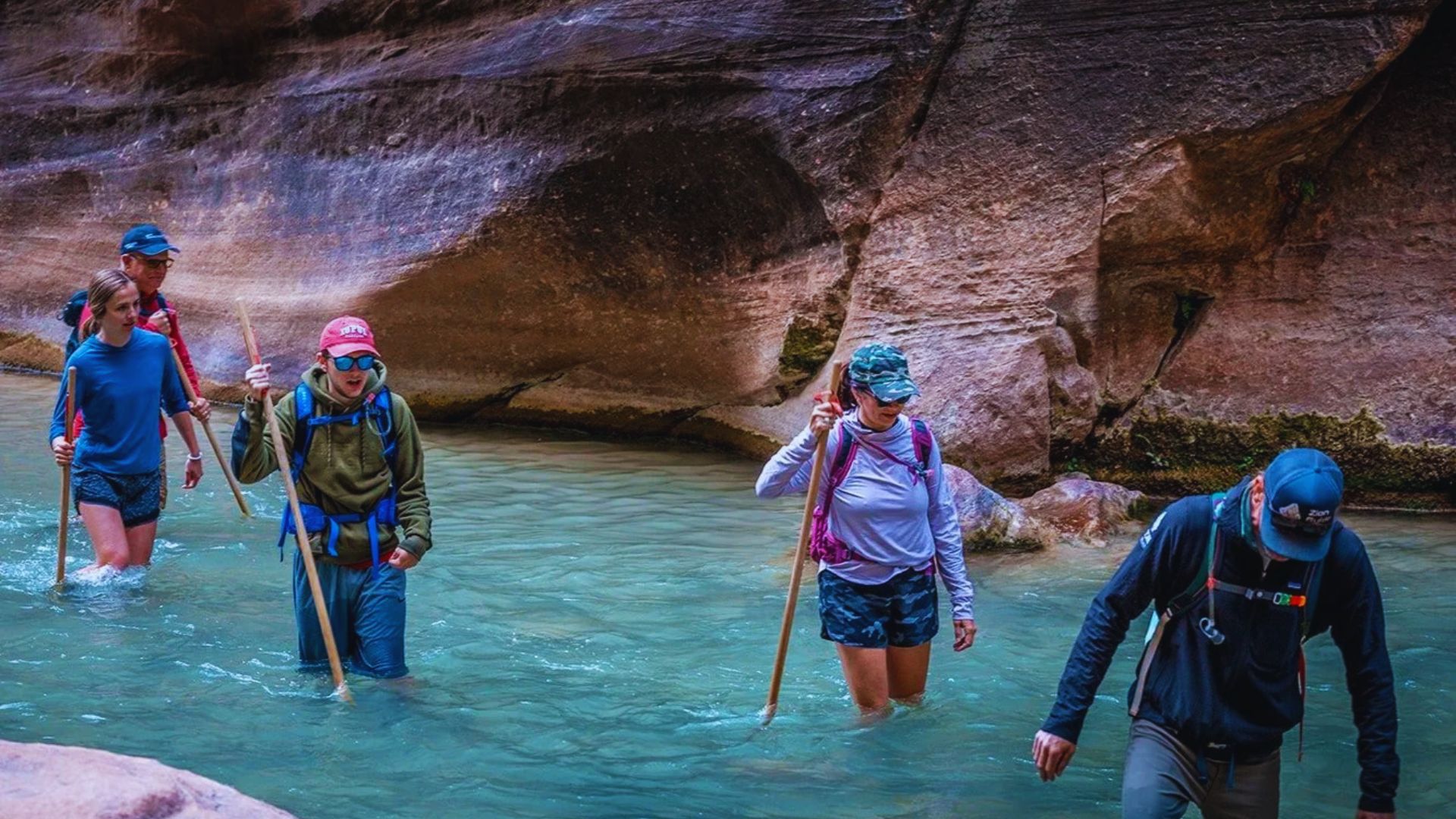 A group of people wading through a river, enjoying nature and each other's company on a sunny day.