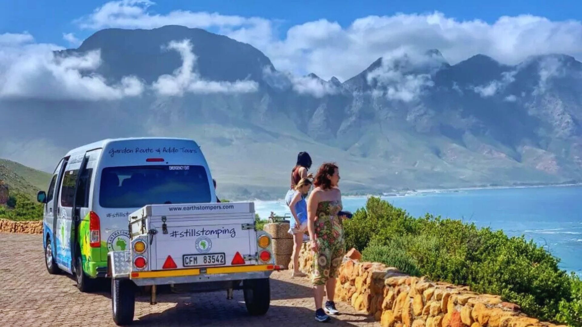 Two people stand beside a van with a mountain backdrop, enjoying the scenic view.