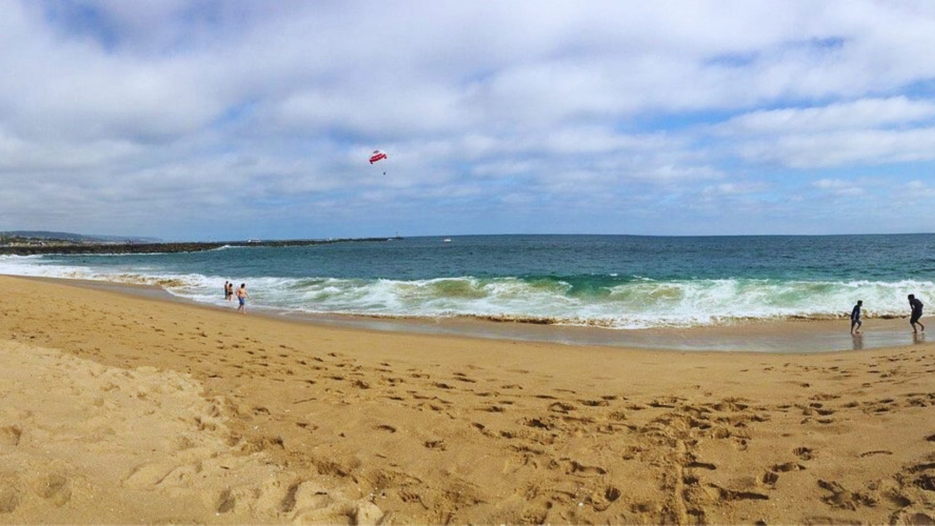 A sunny beach scene with people enjoying the sand and a colorful kite flying high in the sky.