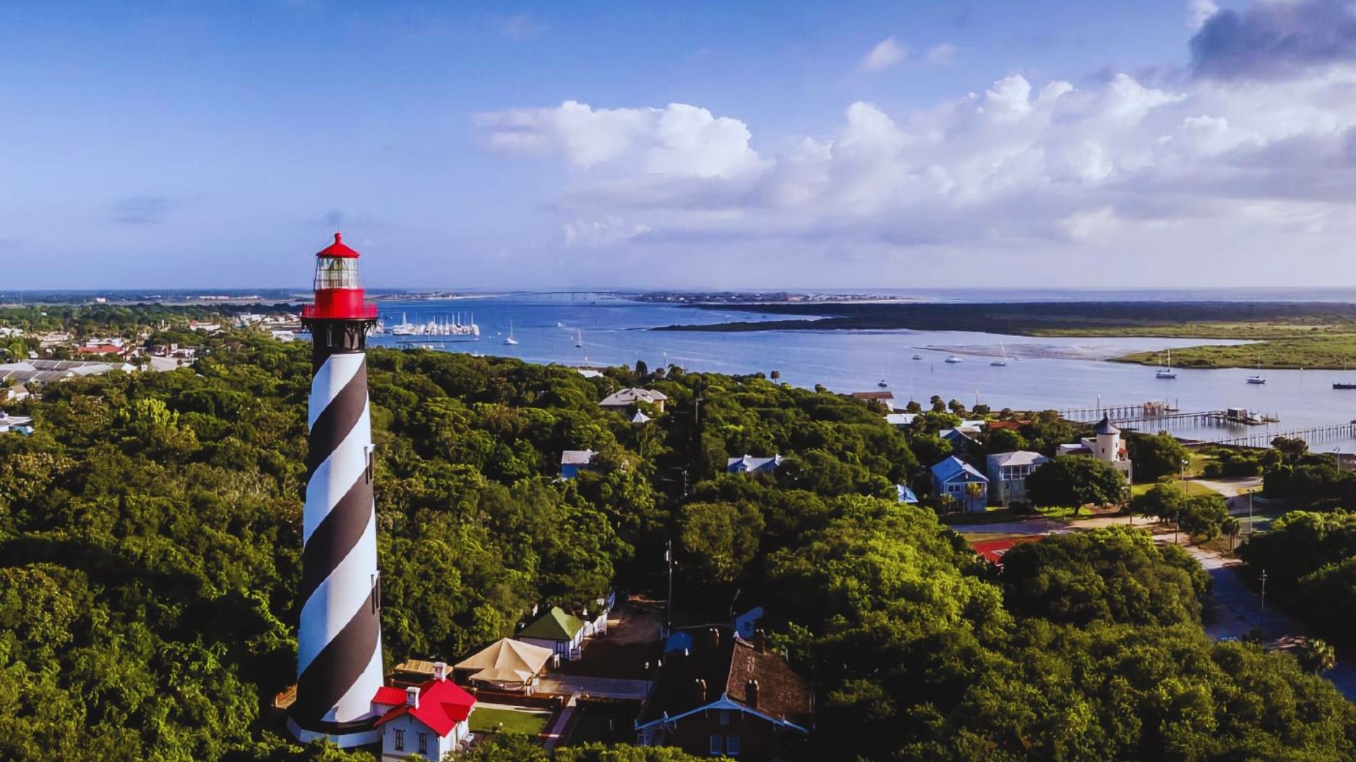 . Aerial view of a lighthouse overlooking a coastal town, showcasing buildings and the surrounding landscape.