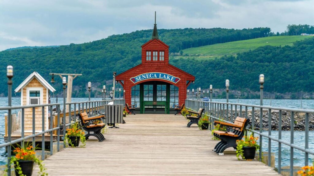 A wooden pier featuring benches and a bright red building in the background against a clear blue sky.