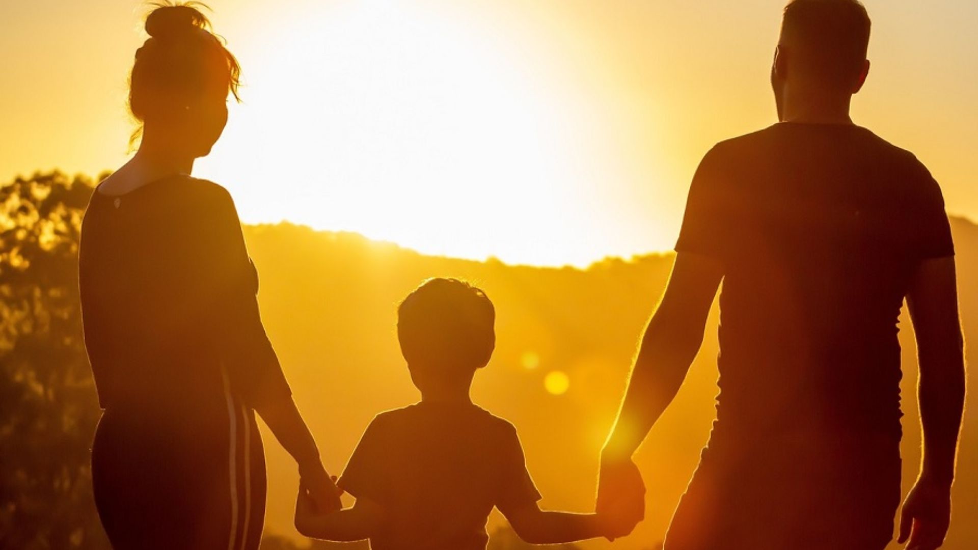 A family of four holding hands together against a vibrant sunset backdrop, symbolizing unity and togetherness.