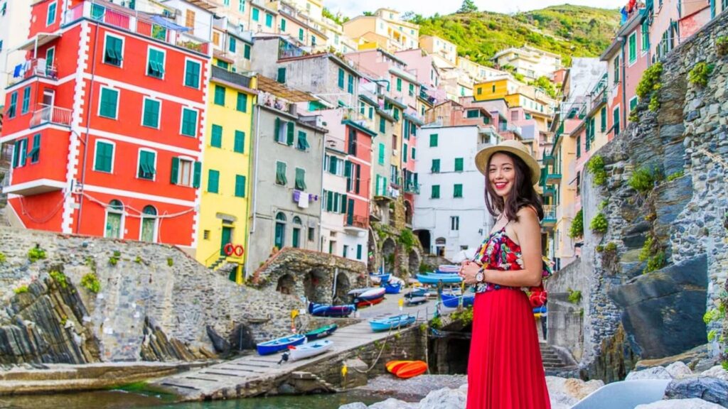A woman in a red dress stands on a bridge, with vibrant buildings in the background.