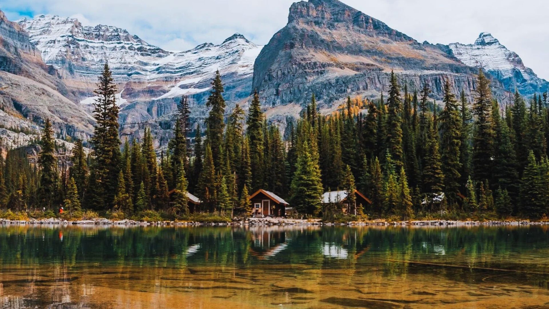 A cozy cabin nestled in the mountains, with lush trees and a peaceful lake nearby.