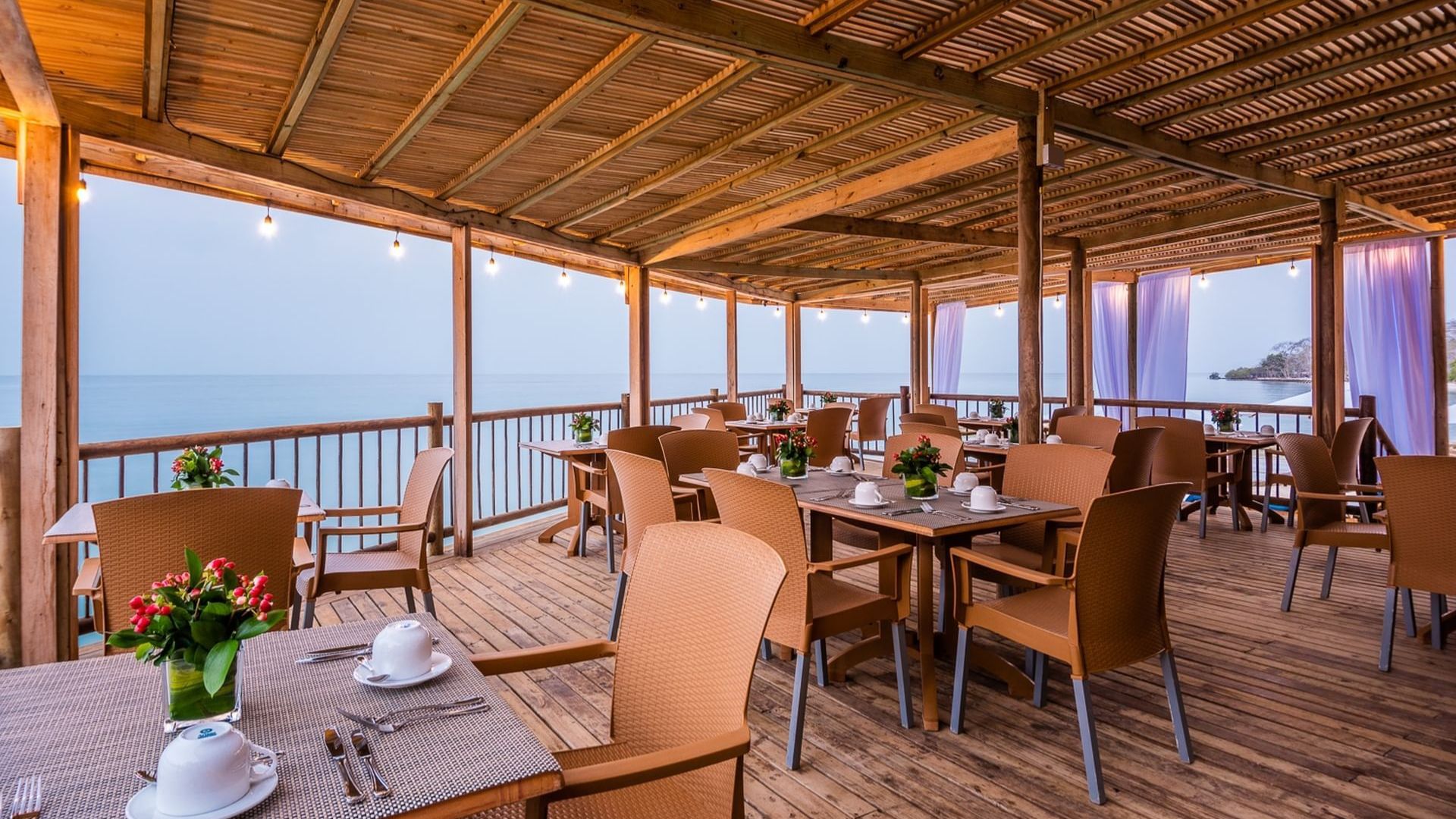 A restaurant deck with tables and chairs, offering a scenic view of the ocean.