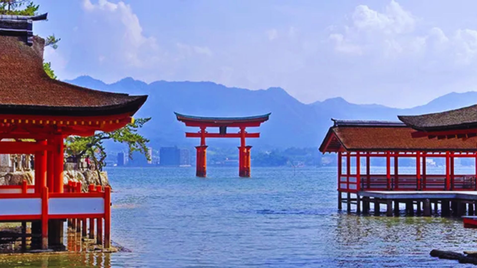 A red torii gate stands in the water beside a mountain, symbolizing a traditional Japanese spiritual entrance.
