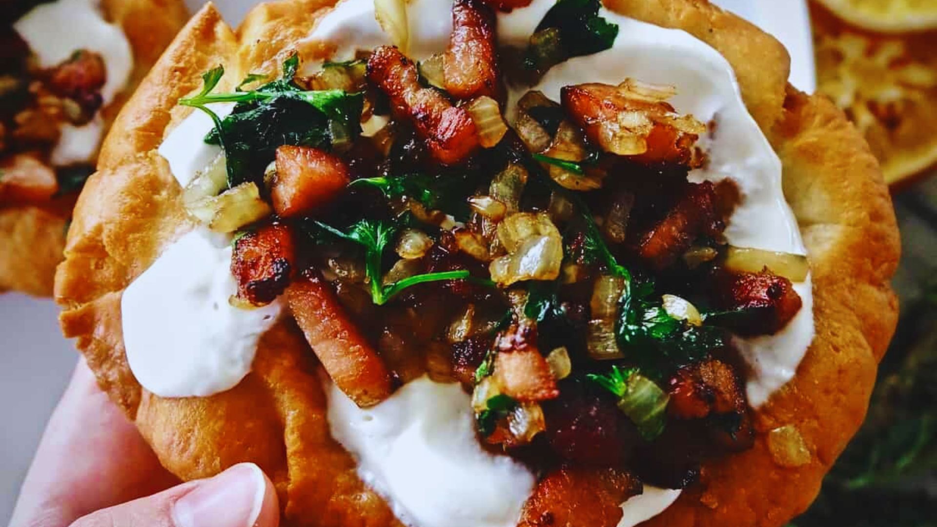 A person holds a small pizza topped with bacon and spinach, showcasing a delicious combination of flavors.
