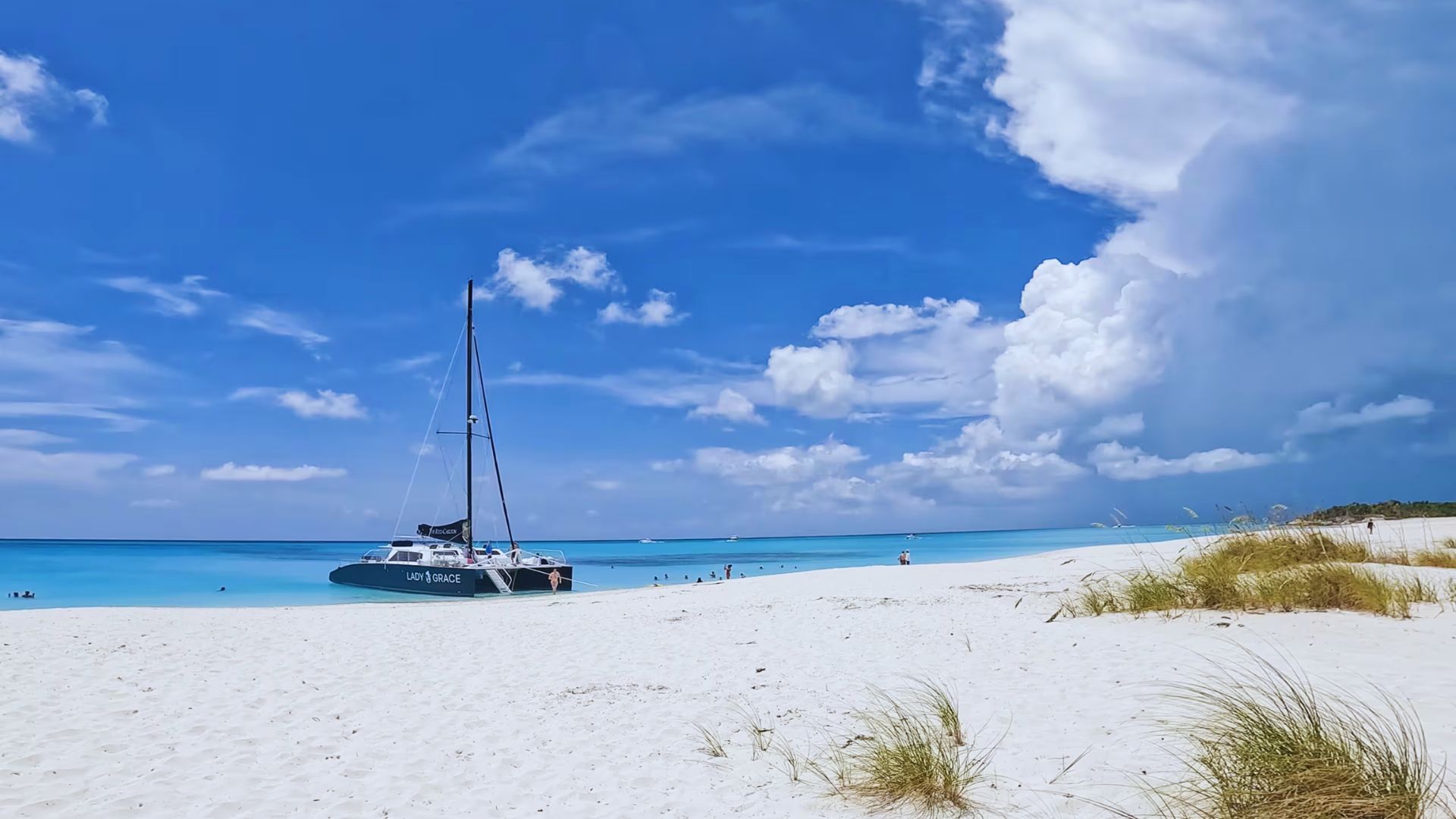 A sailboat anchored on a pristine white sandy beach with turquoise water under a vibrant blue sky. Fluffy clouds in the distance evoke a serene atmosphere.