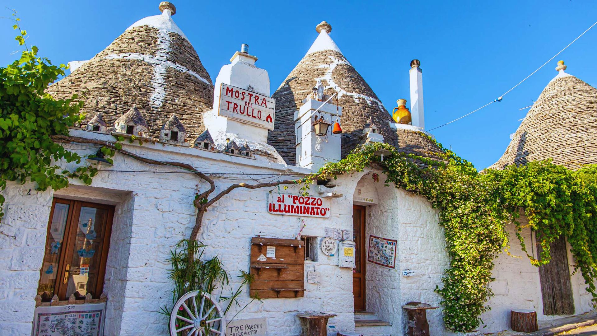 Trulli houses in Puglia, Italy, featuring conical roofs and whitewashed stone walls against a clear blue sky.