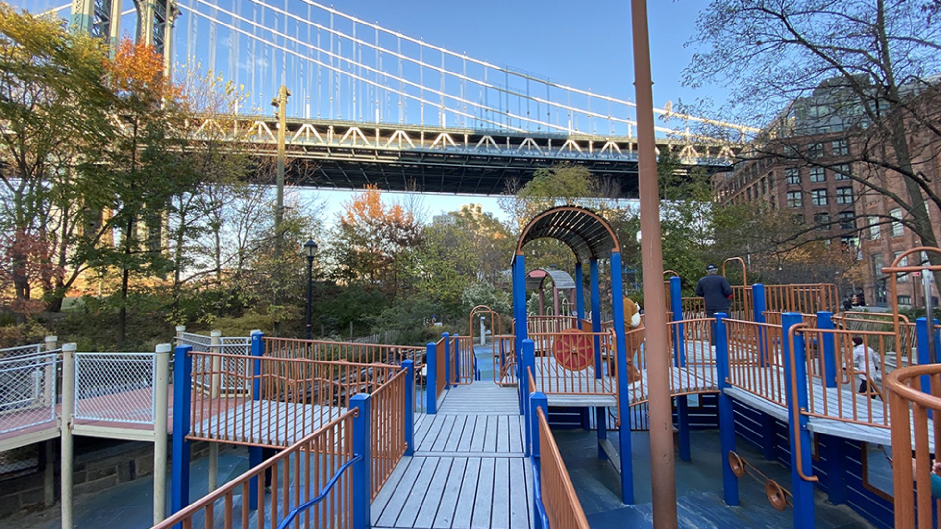 A playground featuring various equipment with a bridge visible in the background.