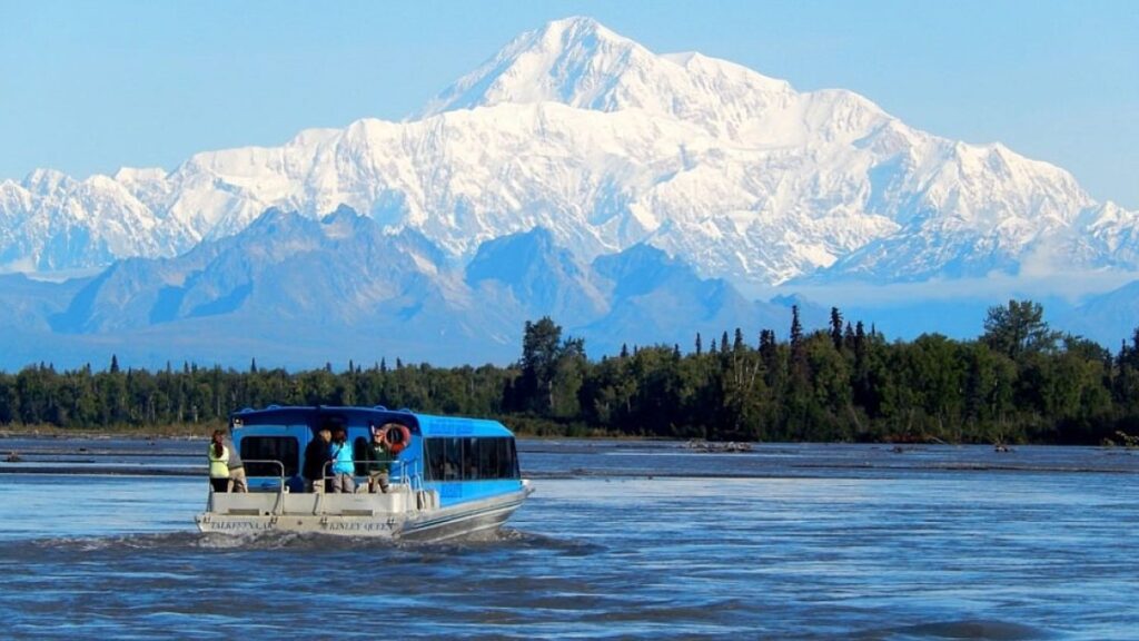 A boat glides down the river, framed by majestic mountains in the background.